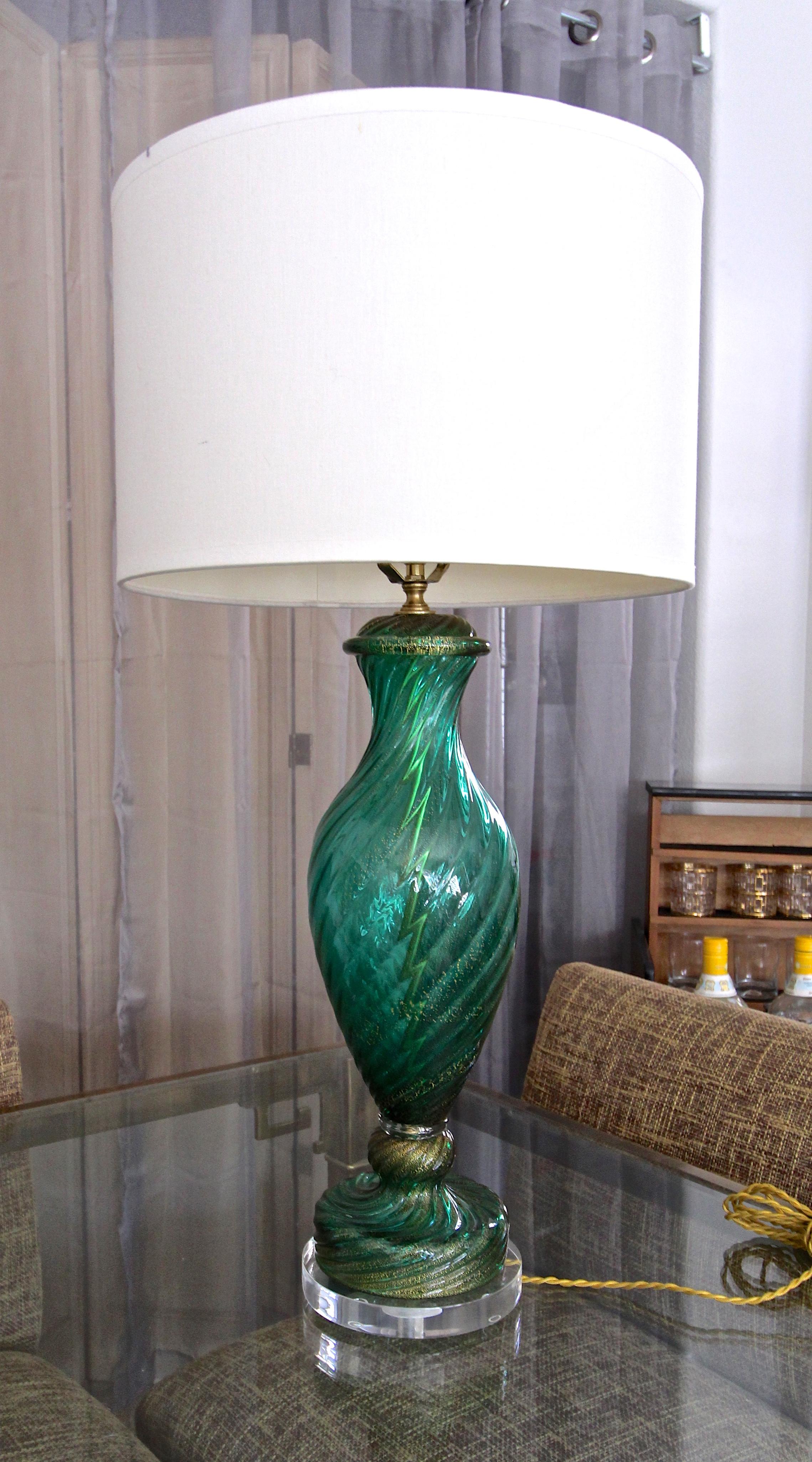 A single tall Italian Murano hand blown emerald green glass with gold inclusions table lamp. Nicely crafted with twisted ribbed baluster form glass detailing. Mounted on acrylic base with brass fittings including 3-way socket and French style cloth