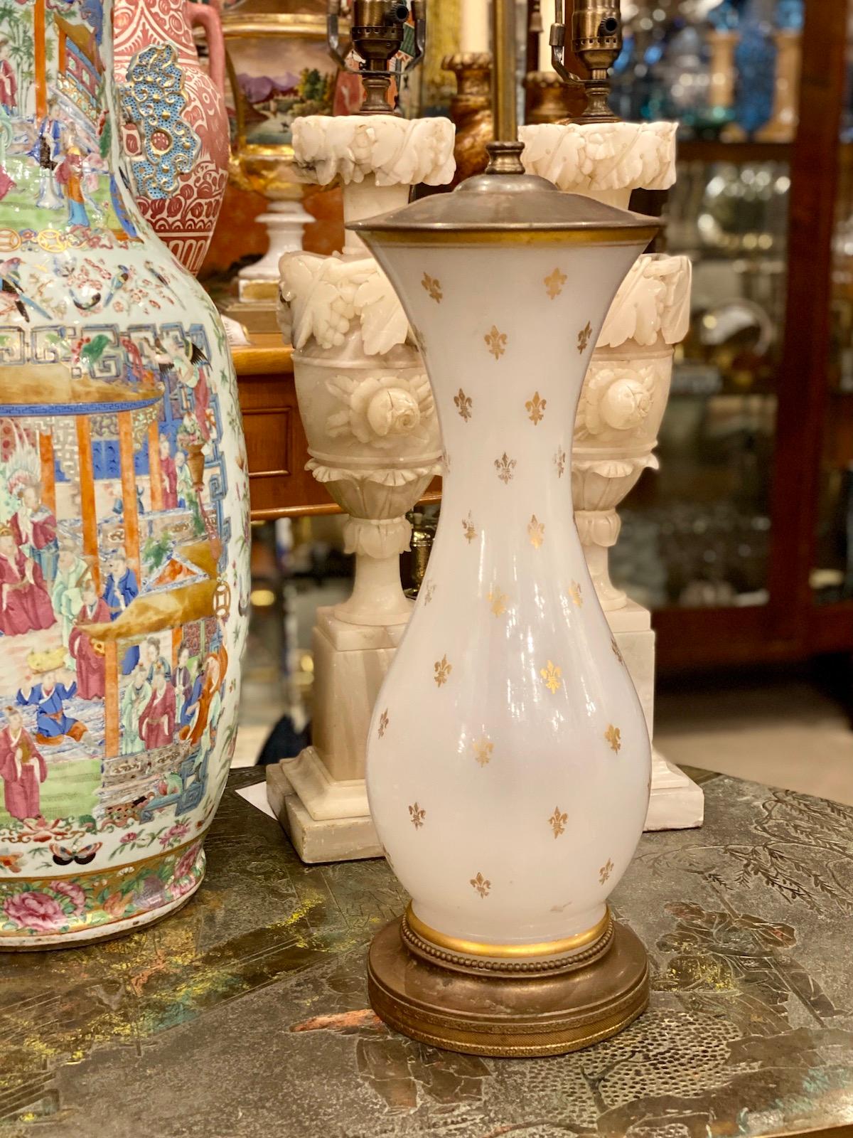 A circa 1920's French opaline glass table lamp with gilt Fleur de Lis details.

Measurements:
Height of body: 18