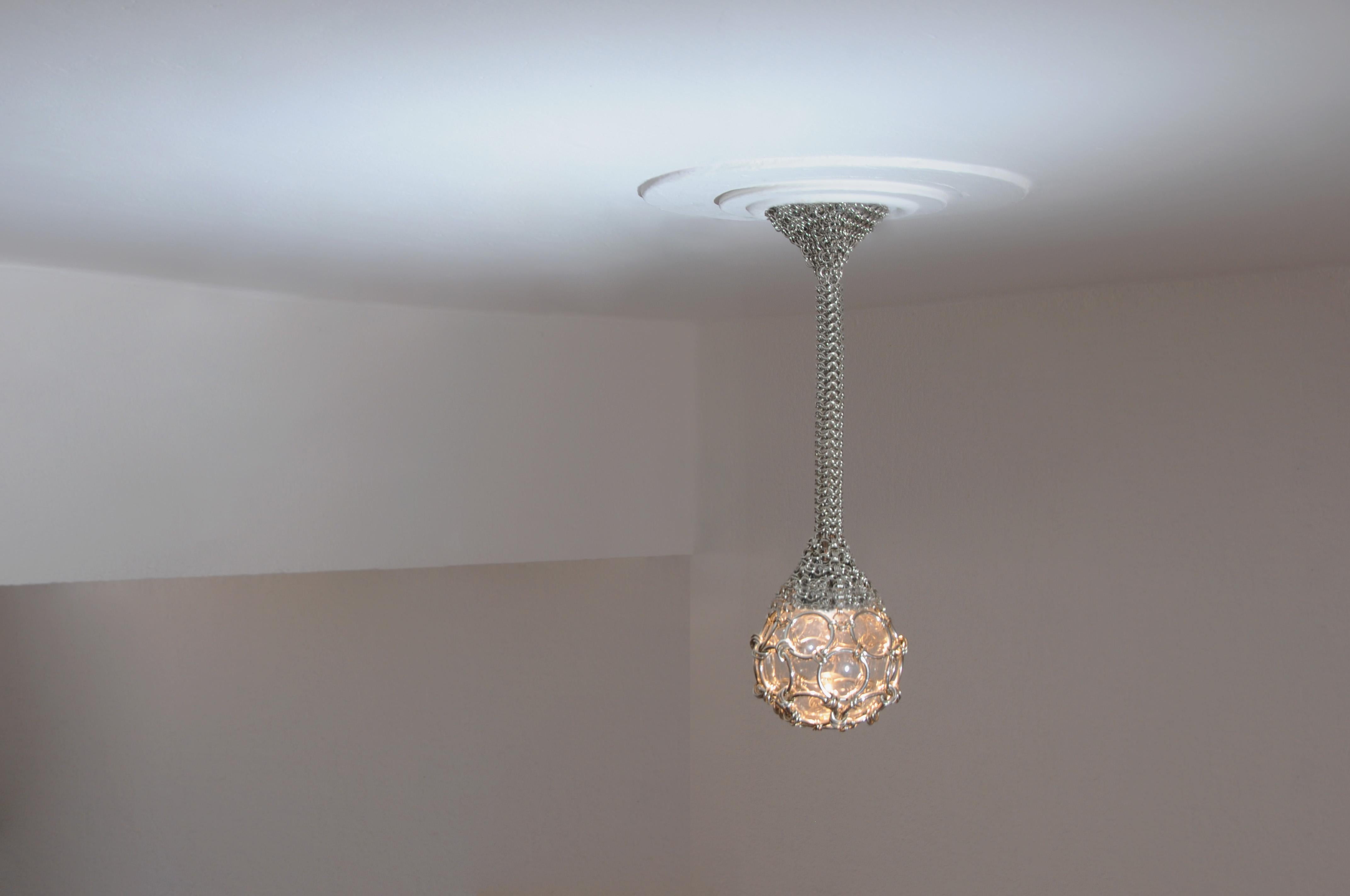 El candelabro escultórico de gotas de cota de malla es una hermosa pieza de luz hecha a mano. Una red de cota de malla abraza el dosel de la lámpara; a medida que el punto se estrecha, la cota de malla se envuelve en una cuerda que cuelga para