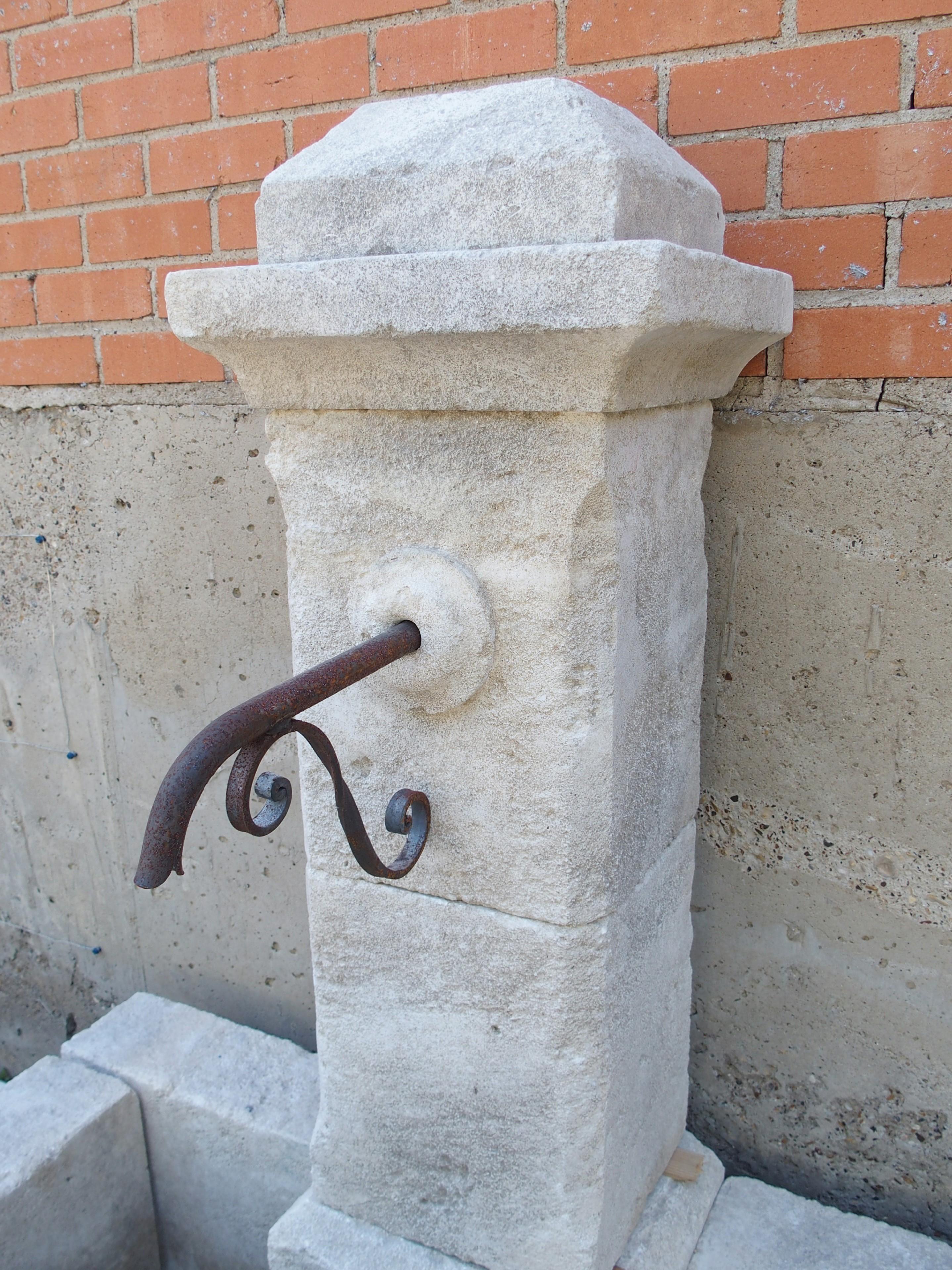 Hand-carved in 11 sections of Estaillade limestone from Provence, France, this single-pillar wall fountain has a wonderful cream patina. A pair of iron bars extend from the front wall of the rectangular basin to the pillar that rises from the back