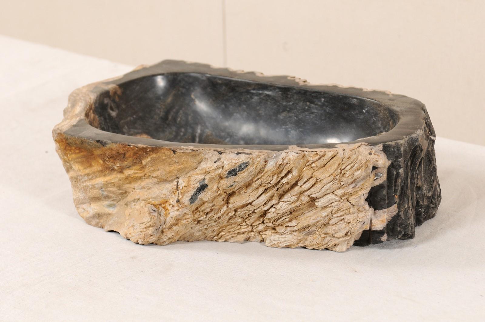 A single petrified wood wash basin. This petrified wood sink has a polished finish basin, making for easy clean-up, surrounded by an unpolished, natural textured exterior. The colors are primarily black with brown veining within the basin, and
