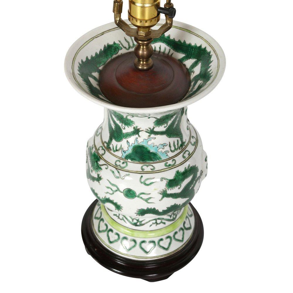 A vintage single porcelain Asian lamp on a wood base with a dragon motif.  A fusion of traditional elegance and artistic craftsmanship, this captivating lamp seamlessly blends the timeless allure of porcelain with the rich symbolism of a green