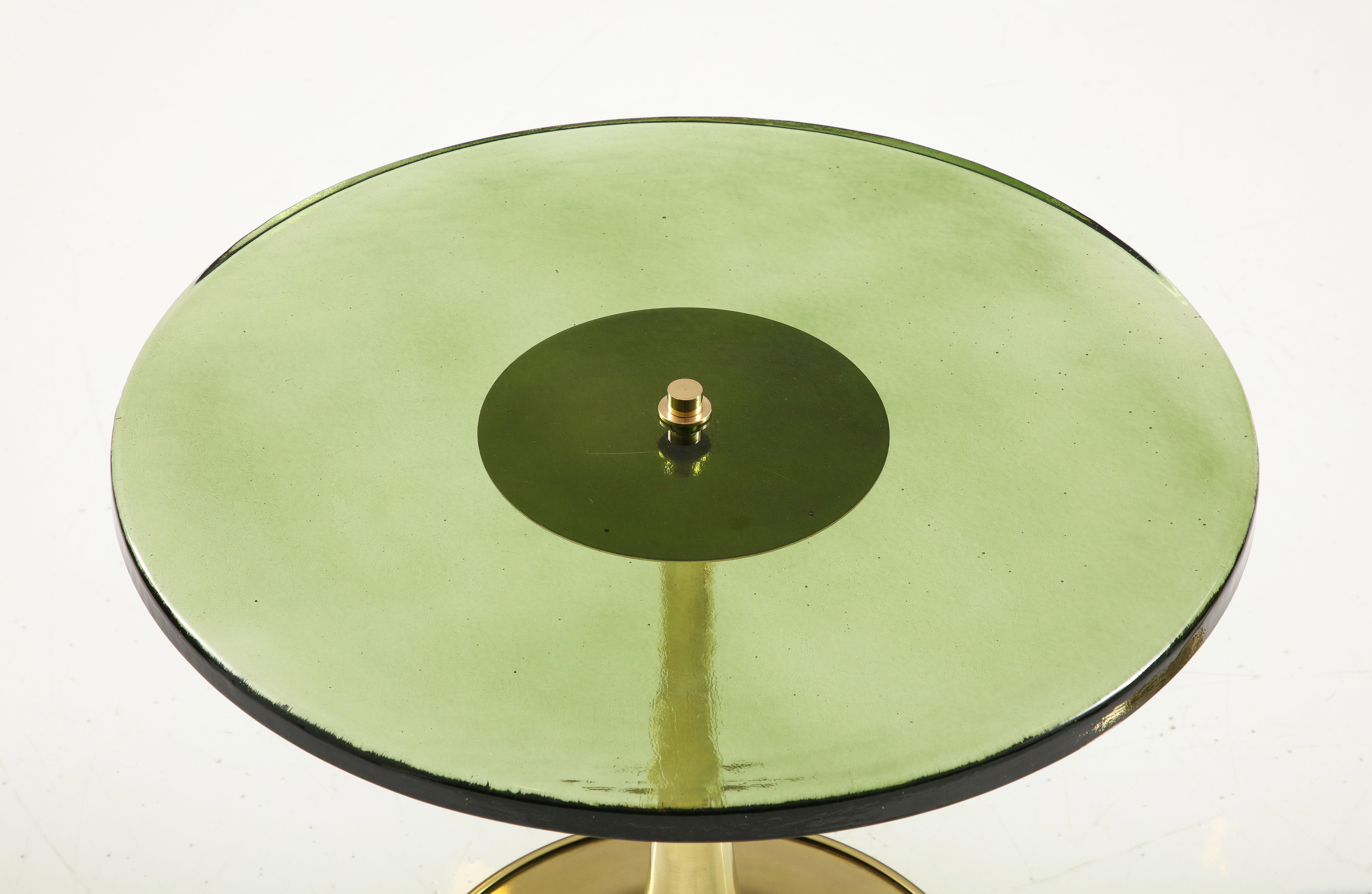 Round green hue murano glass and brass martini or side tables, Italy, 2023. Hand-casted 1 inch thick, solid, deep green colored murano round glass top sits atop a hand turned, trumpet-shaped brass base. A modern flat top brass finial screws the
