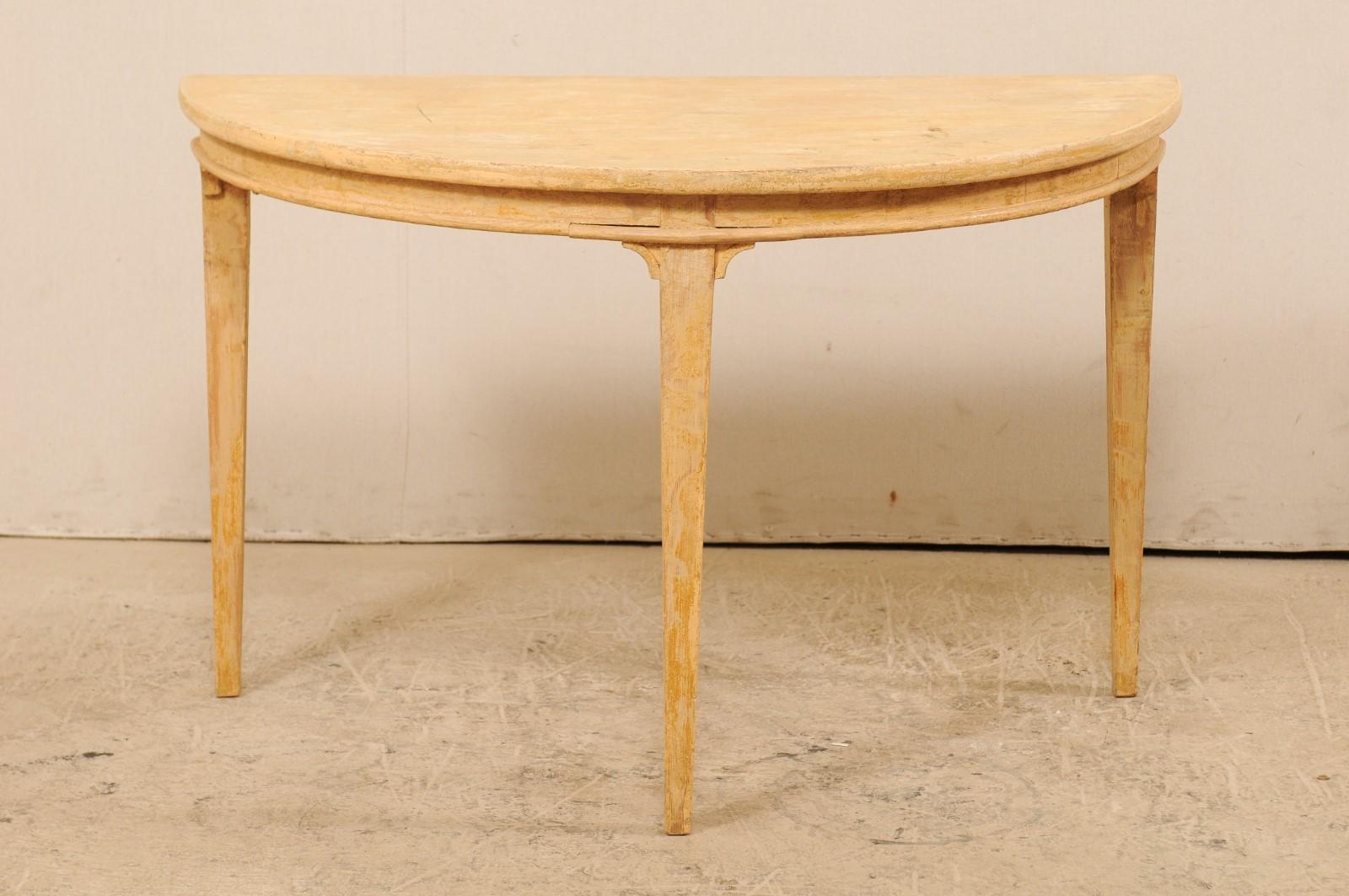 A single Swedish wooden demilune table from the 19th century. This antique table from Sweden features the typical half moon shaped top, over a rounded apron, and raised on squared and tapered legs. Small brackets are positioned where each leg top