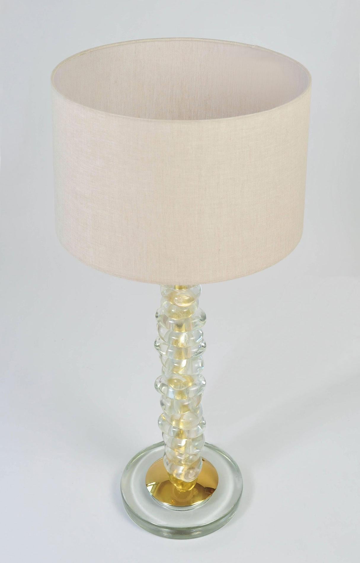 Lampada da tavolo alta e contemporanea con 15 ciottoli trasparenti di Murano scolpiti a mano e lisci. Ogni ciottolo è intervallato da uno strato di ottone. Poggia su una base circolare in vetro con dettagli e piedi in ottone. L'effetto complessivo è