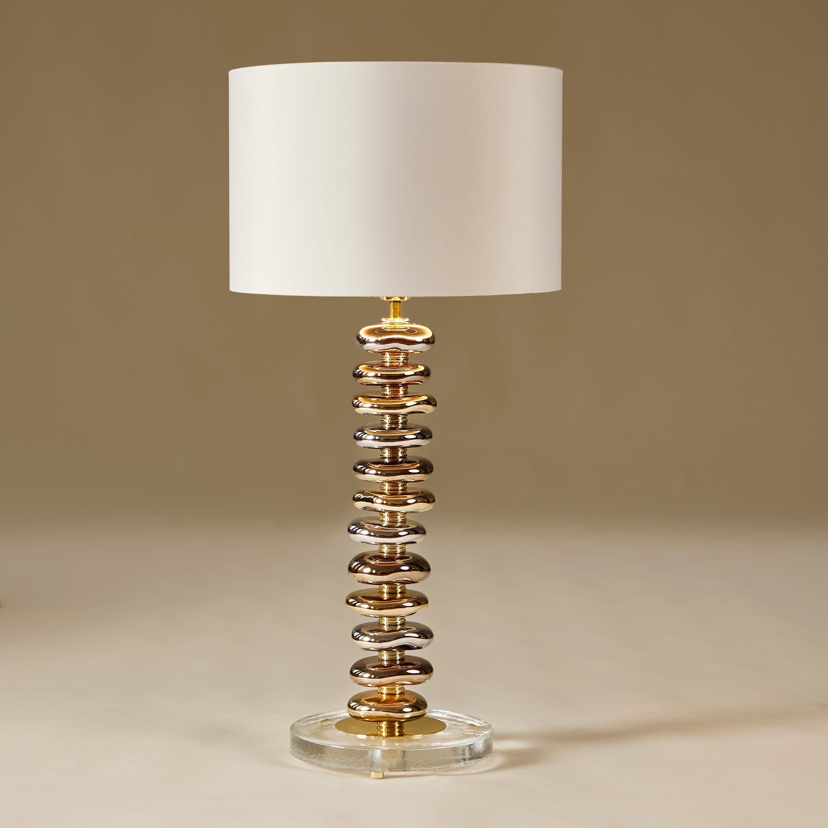  Each lamp consists of 12 handmade smooth sculptured Murano pebbles in metallic shades of gold, silver and bronze. Each pebble is interspersed with a tiered layer of brass. Sits on circular glass base with brass detailing and feet. The overall