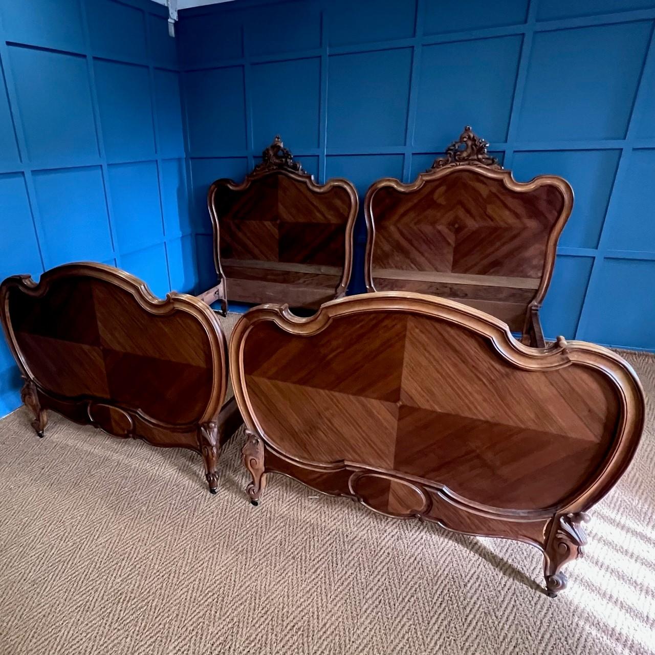 Beautiful pair of statement walnut Louis XV single beds featuring the classical quarter veneer panels. Dating from circa 1900 these curvaceous beds have the exquisitely carved classical crest and are grounded by small brass cuffed castors providing