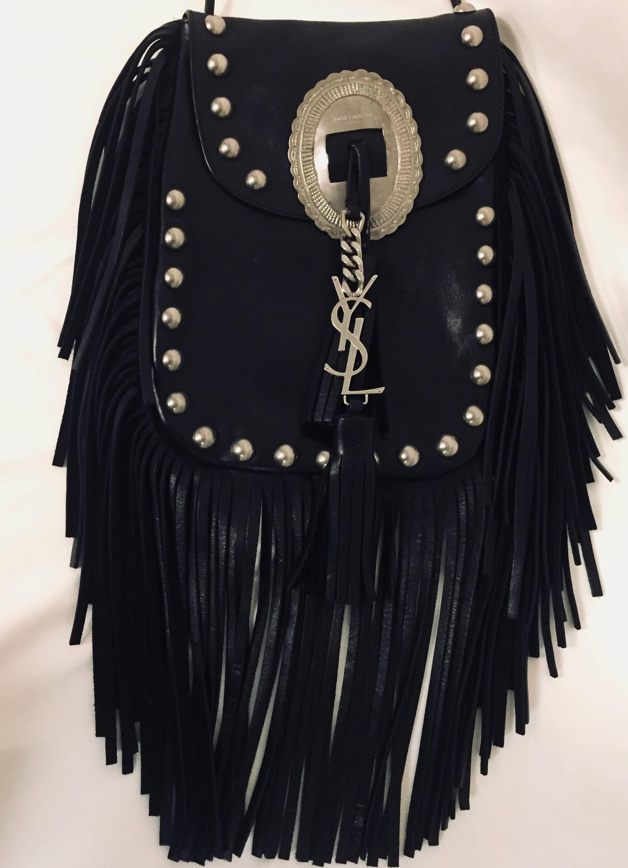 This Saint Laurent black leather Anita flat bag features antiqued silver tone hardware and tonal stitching throughout.  For closure one flap with  logo Saint Laurent plaque and a leather tassel and YSL charm in silver tone.  Tonal suede fringe