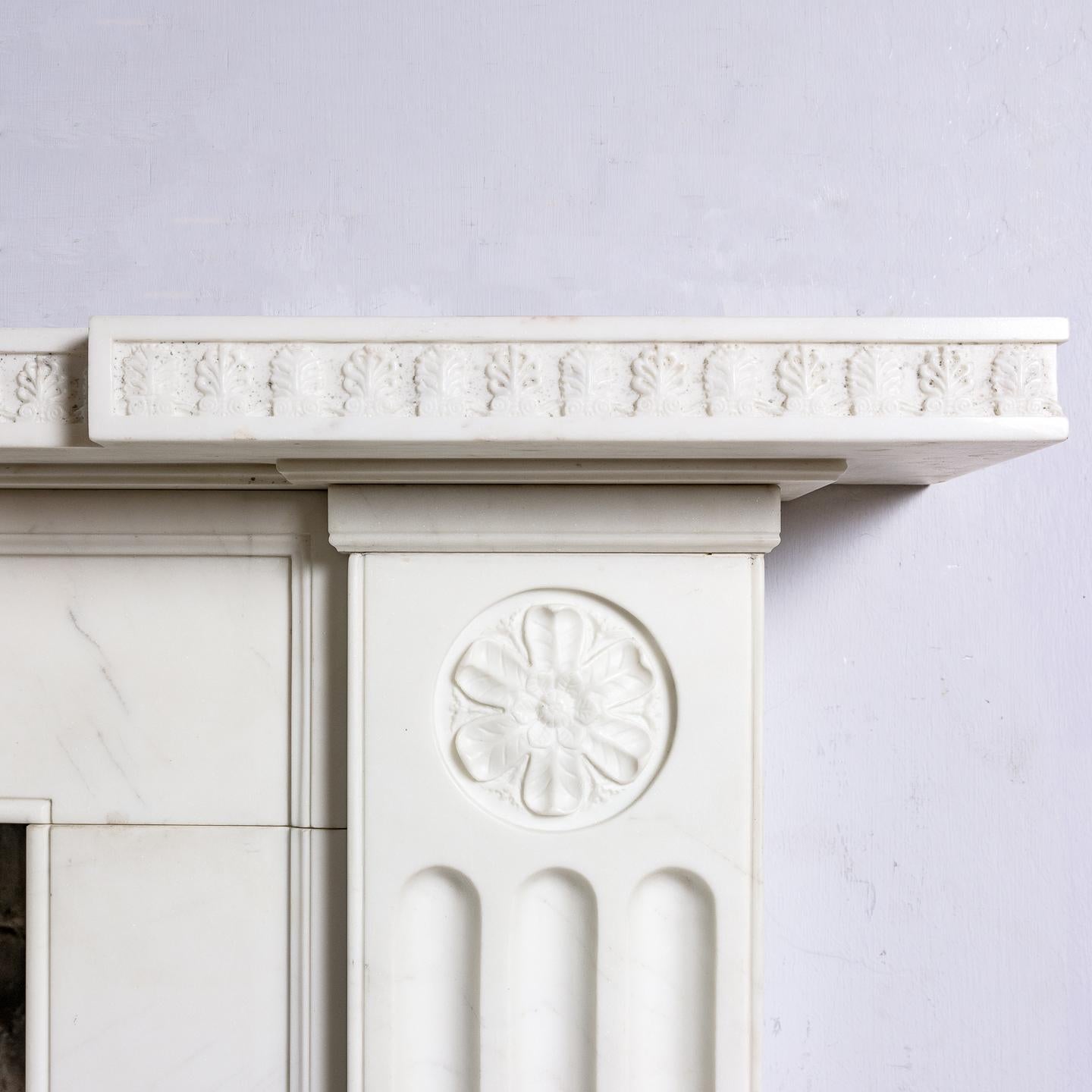 A Regency style white marble fireplace, to a design by Sir John Soane, the inverted breakfront shelf above frieze with a band of anthemion carved in relief, the fluted jambs headed by rosette roundels, made recently.