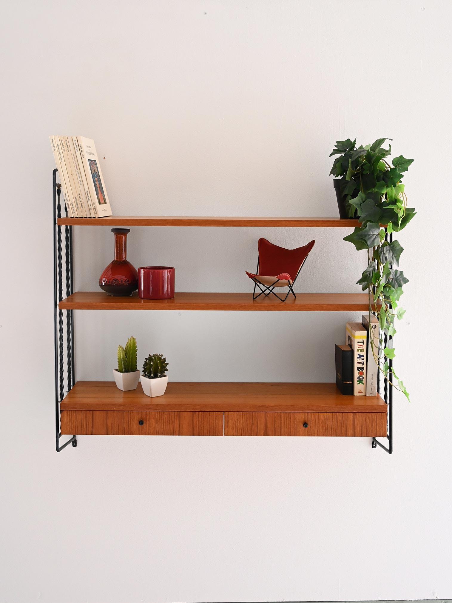 Etagère murale vintage avec cadre métallique, trois étagères en teck et module pratique avec tiroirs intégrés.

Etagère scandinave vintage en teck, datant des années 1960, avec cadre mural en métal peint en noir. Les étagères légères mais solides