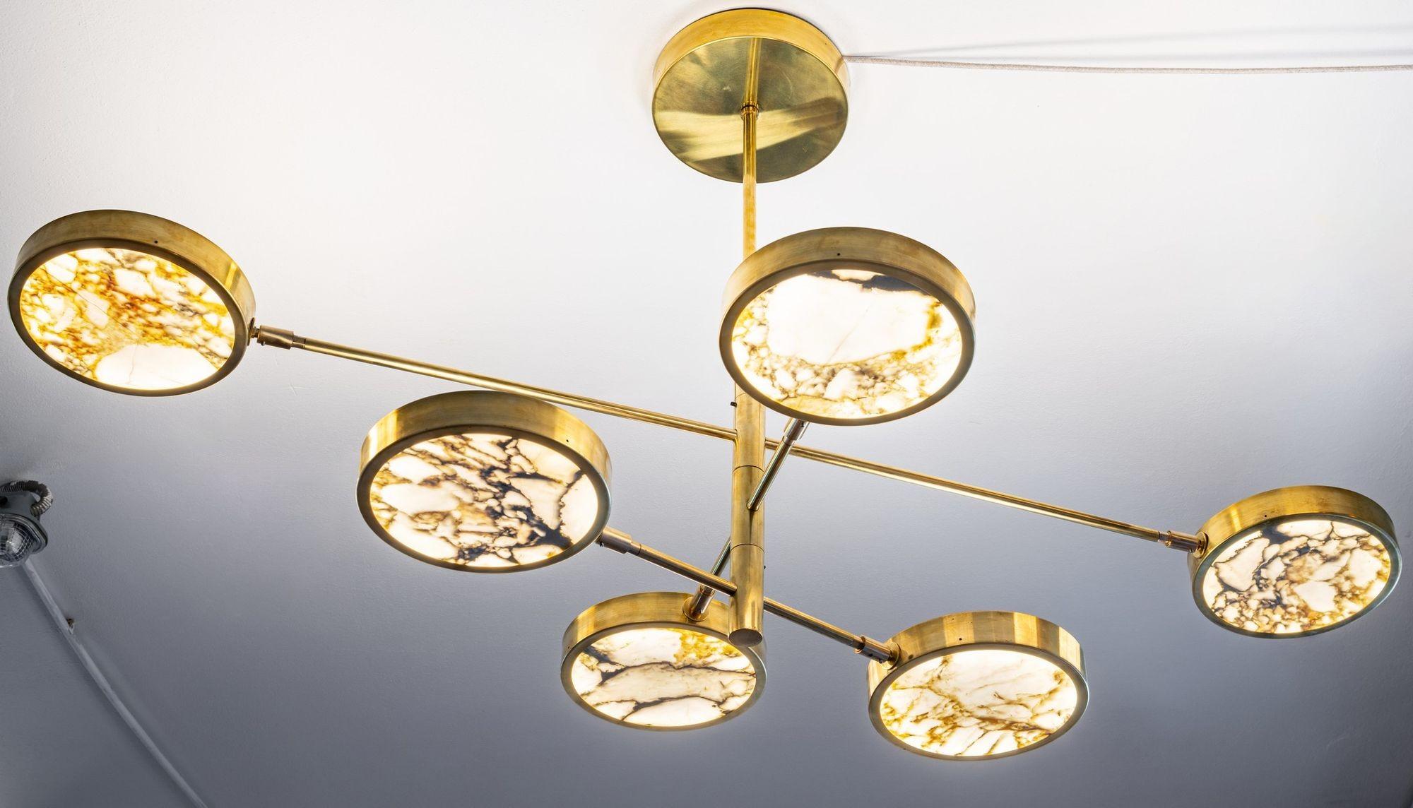 Our luxury chandelier showcases thin cut Calacatta gold marble - an elegant rare marble extracted from the Tuscan Alps. This prestigious Italian marble stands out among others with its veining, transitioning from a warm gray to a resplendent golden