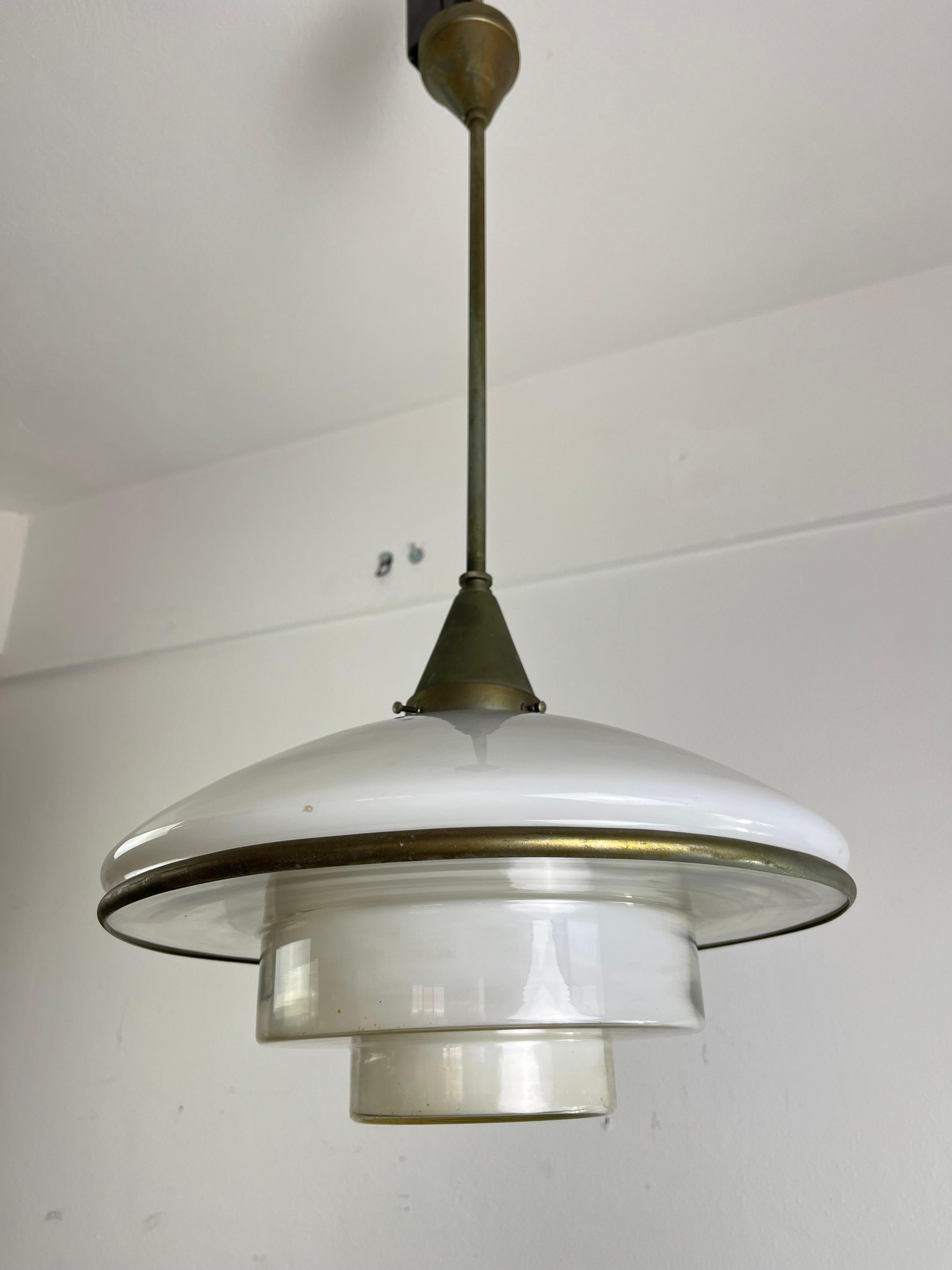 Questa lampada a sospensione è stata progettata da Otto Müller nel 1931 e prodotta da Megaphos/Sistrah Licht GmbH in Germania. È composto da due paralumi in vetro uniti da una cinghia cromata. Il paralume superiore è in vetro opalino bianco; il