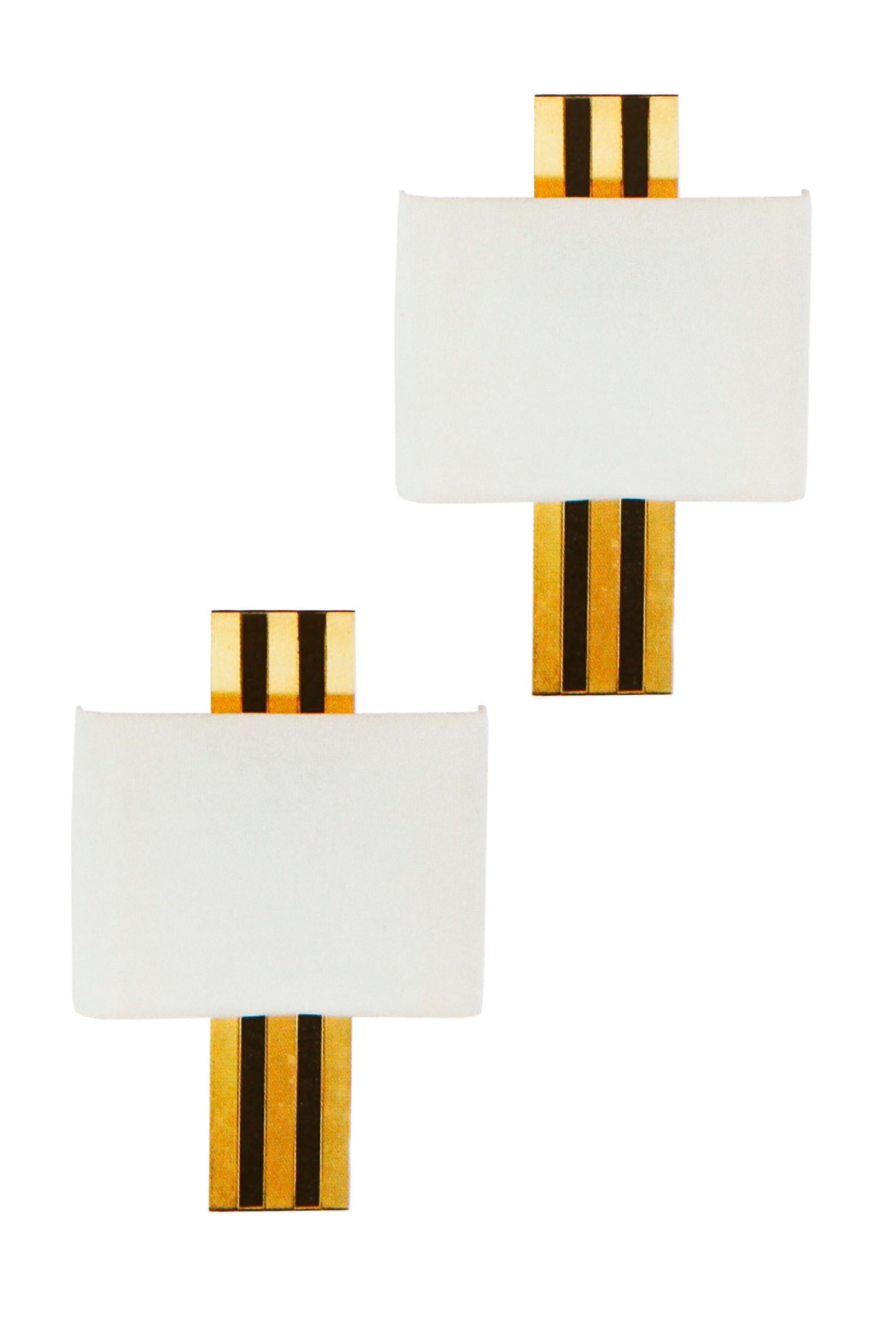 A set of six 20th century brass and black plastic three light wall scones by Willy Rizzo. Each with pierced rectangular back issuing a horizontal bar with three lamp sockets. With white cotton shades, circa 1970.
