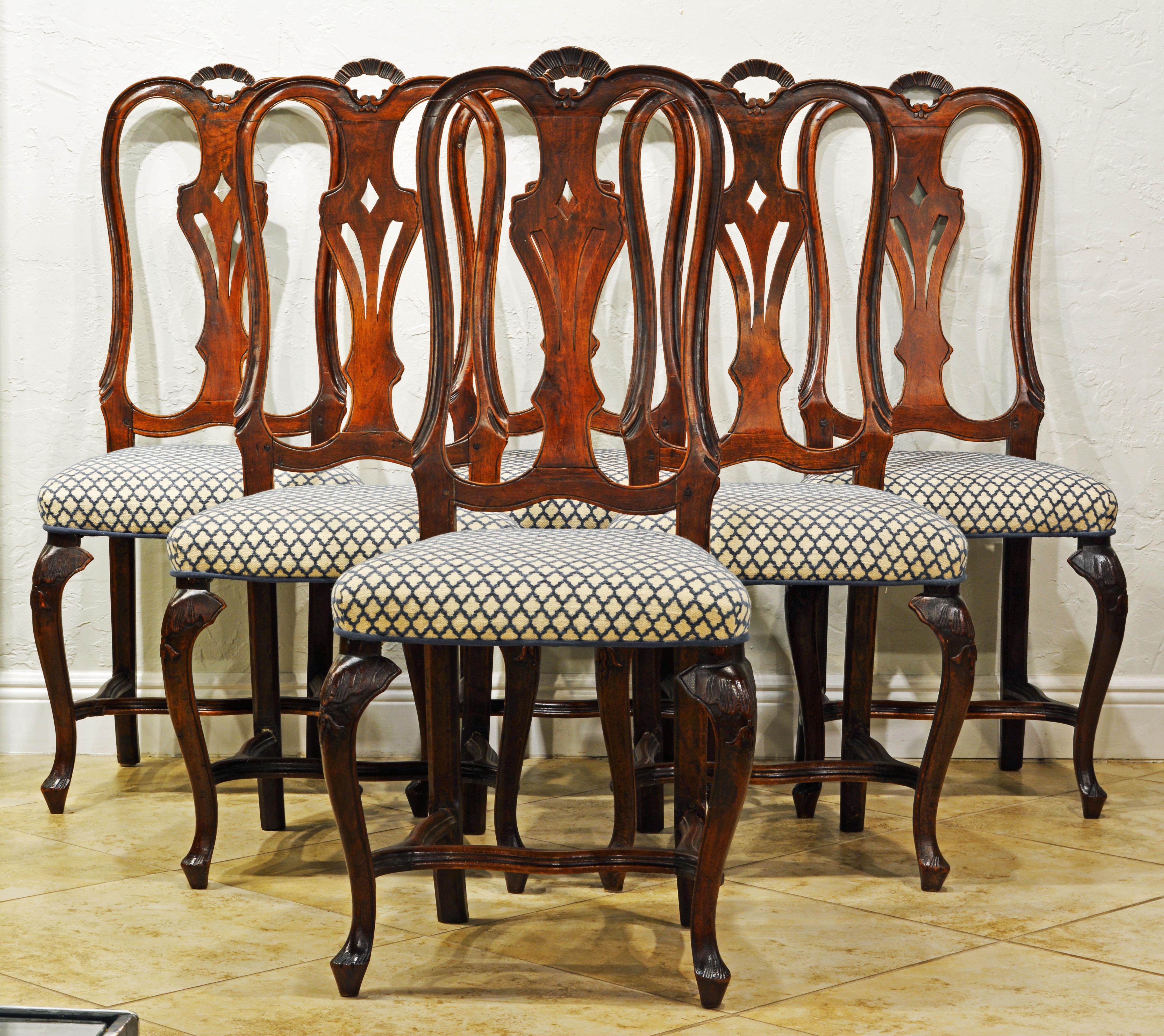 These late 18th century Italian Rococo or Louis XV style dining chairs feature beautifully curved back frames with small carved top arches, carved openwork splats, upholstered seats and carved cabriole legs united by low curved stretchers.