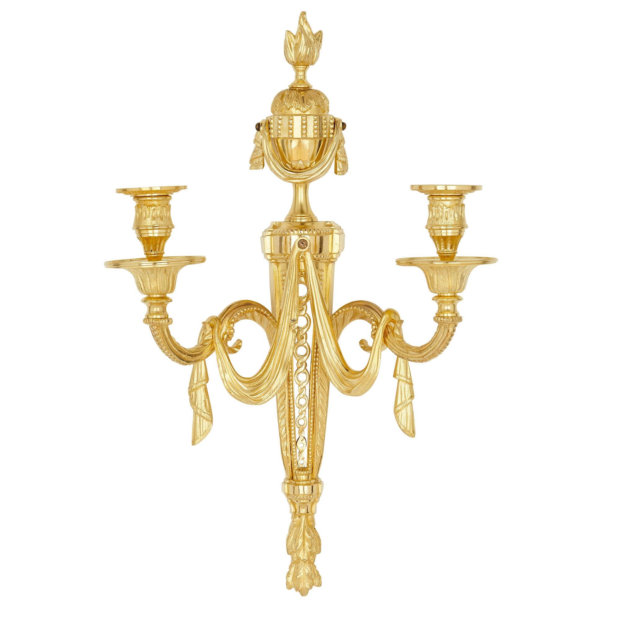 Each of the six gilt bronze sconces (or wall lights) is composed of a pointed central stem, two arms which hold the lights, and a flaming urn finial. 

The lower part of the stems are cast as groups of acanthus leaves, which point downwards. The