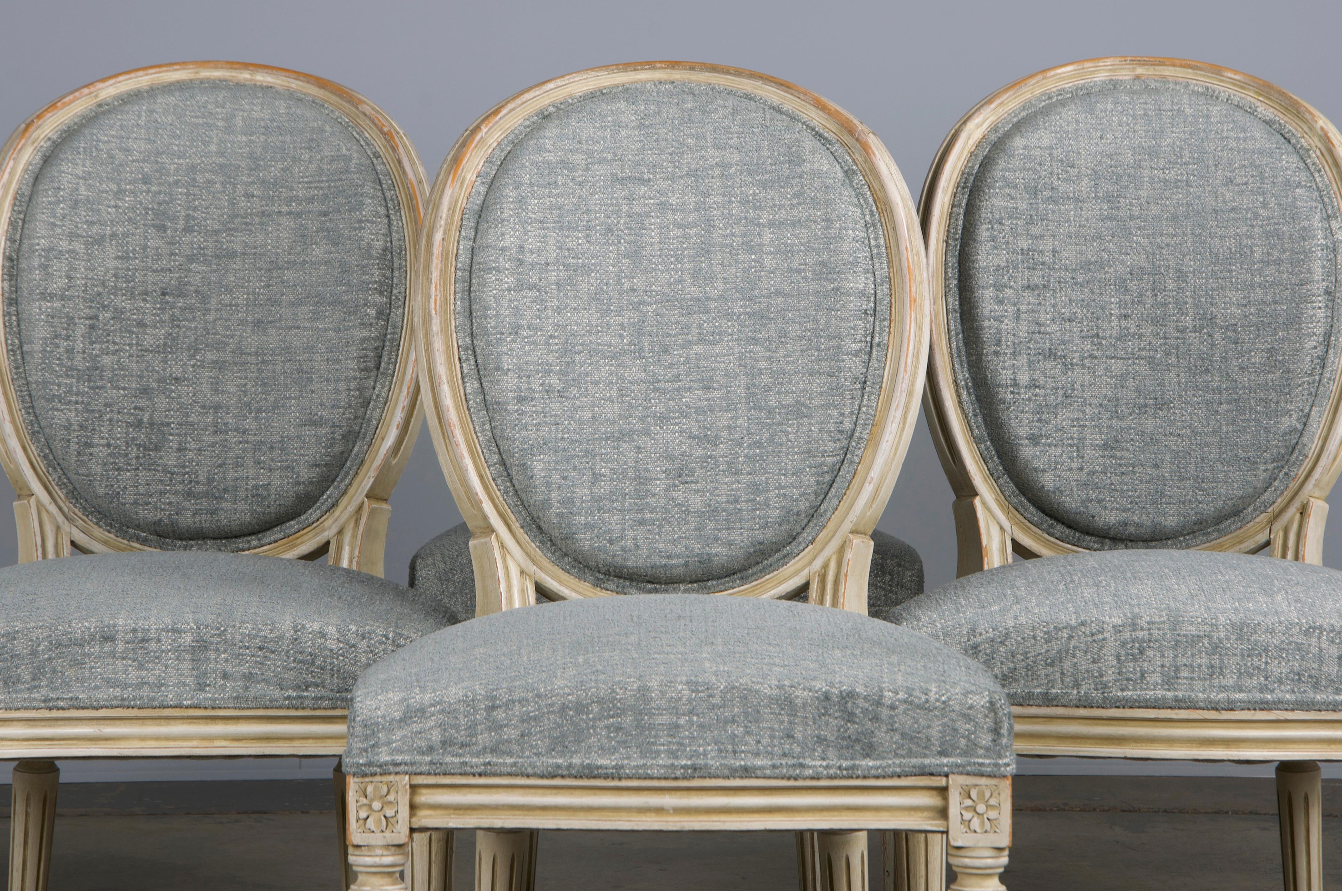 An exquisite set of six antique French dining chairs made in the style of Louis XVI, sourced from Provence, France. Each chair features a hand-molded frame adorned with an oval-shaped medallion back. Hand-painted in creamy, antique white paint
