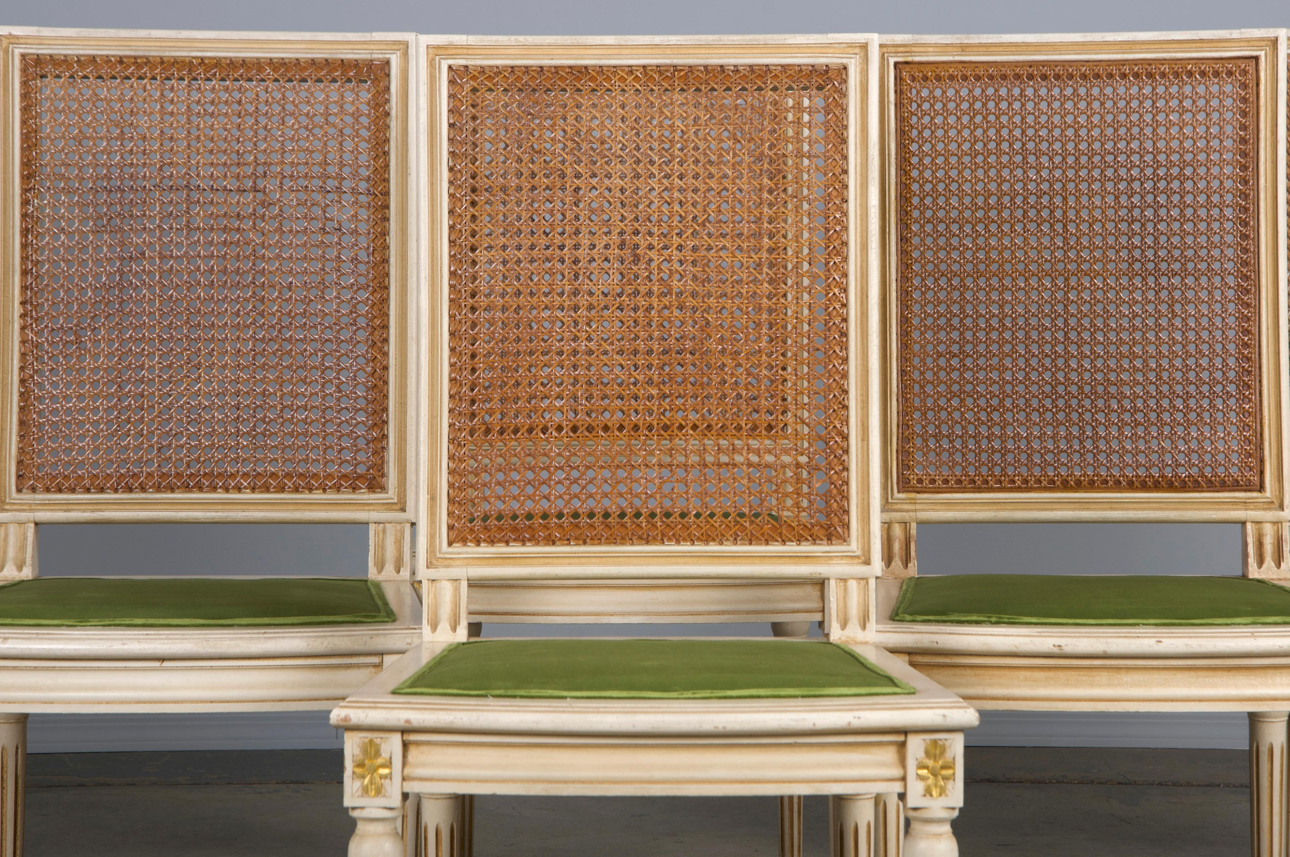 An elegant set of six late 19th-century dining chairs crafted in the Louis XVI style, sourced from Provence, France. Each chair features a hand-carved frame with a tall, square-shaped cane back and is finished in creamy antique white paint that