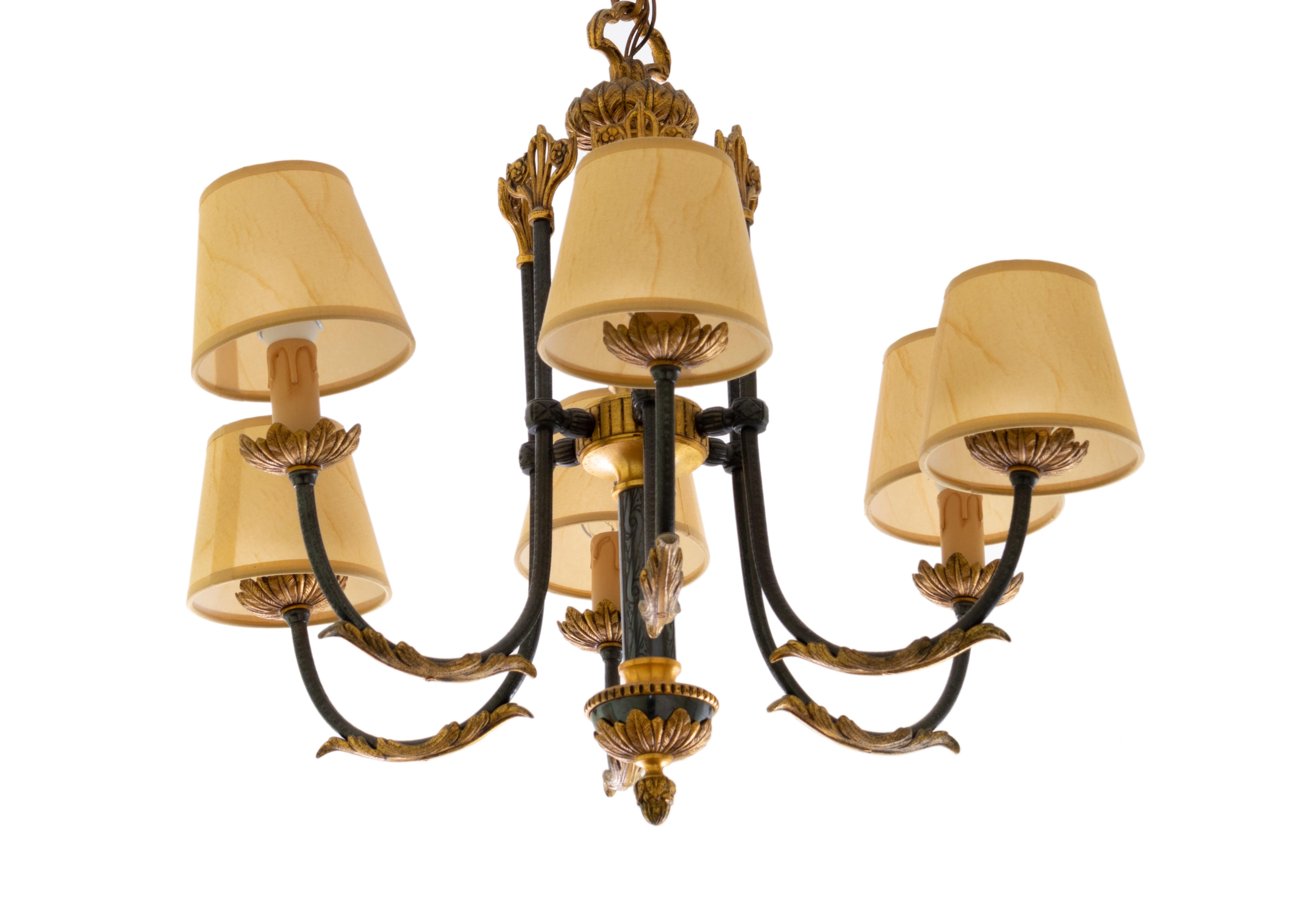 The fully adorned bronze and gilded metal chandelier boasts six arms, gillded chains, each adorned with a lamp. It features six points of light in a sleek black finish, accompanied by individual fabric lampshades, a twist of french Louis XIV style