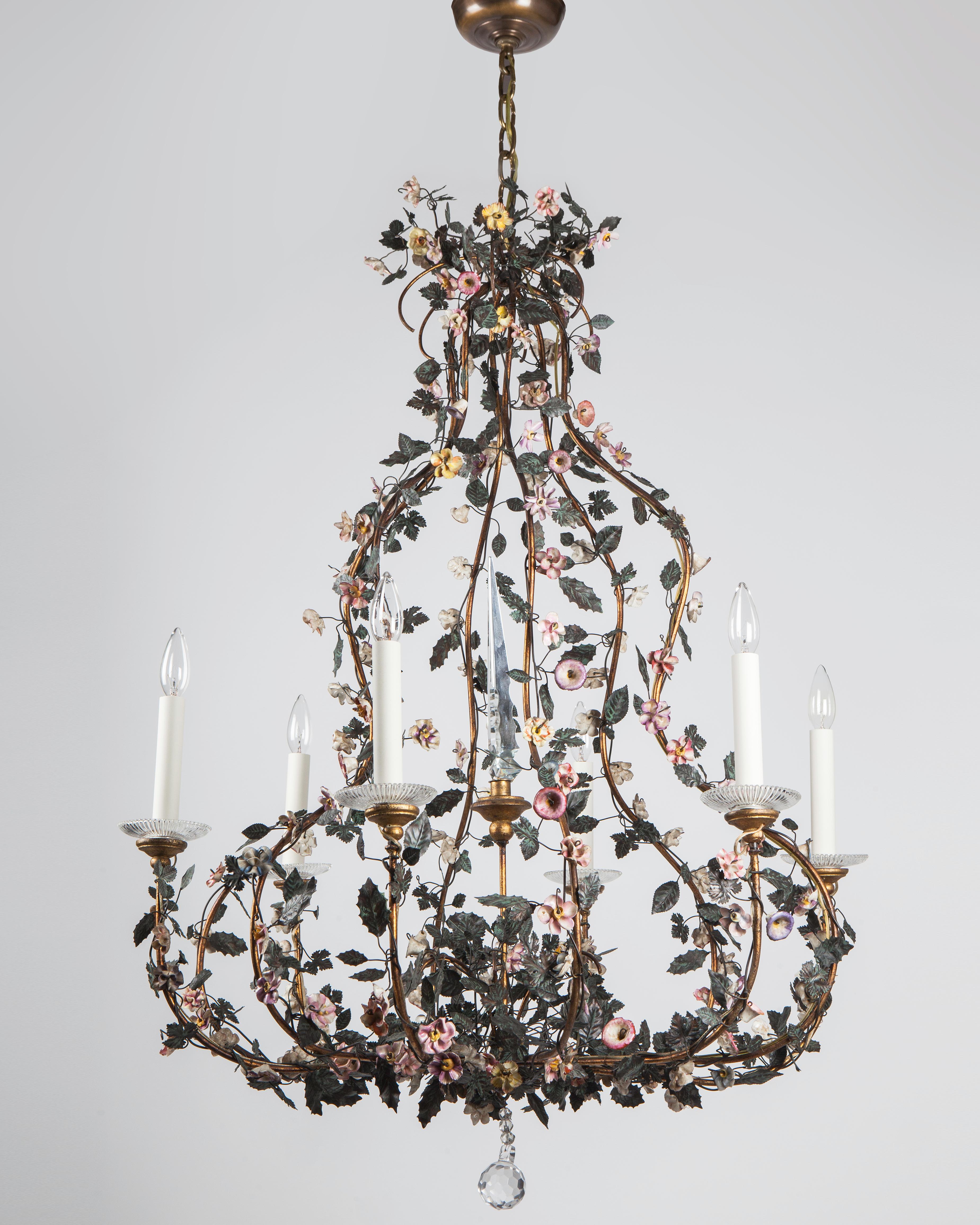 AHL4212
A large six arm vintage tole chandelier having a darkened iron openwork lyre form frame detailed with hand-painted vines, sprays of leaves, and colorful porcelain flowers. Sparkling crystal details catch the light throughout including
