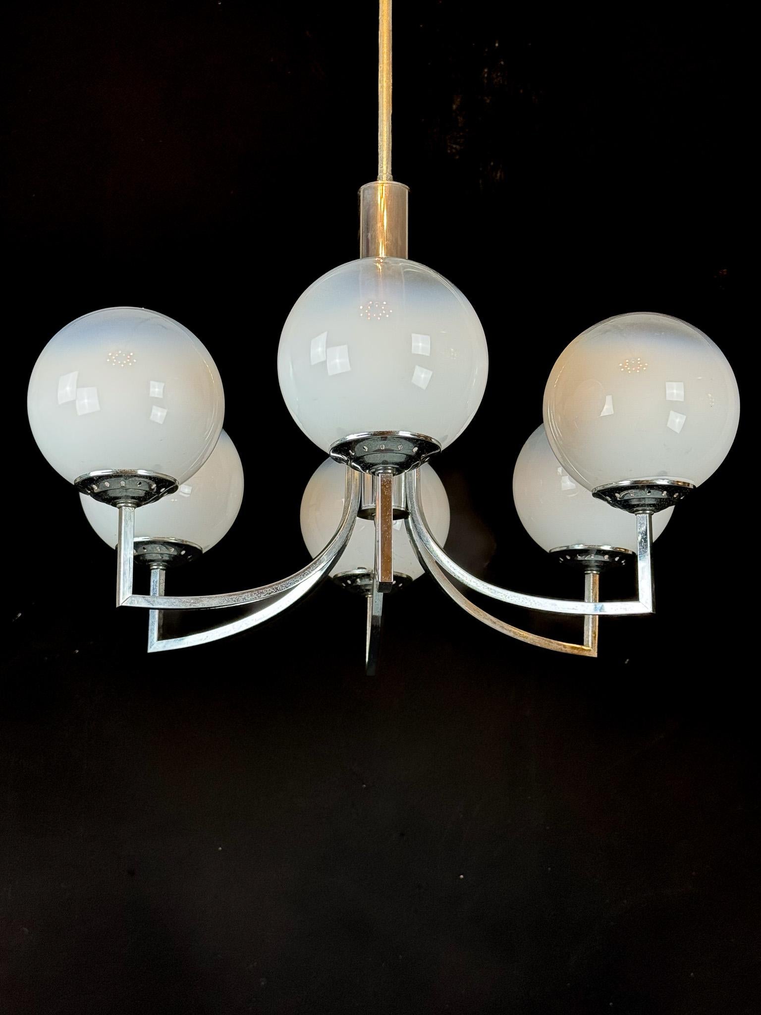 Elegant six-arm chandelier featuring hand-blown Murano glass spheres mounted on a polished chrome structure. The white gradient glass globes diffuse a soft, warm light, creating a sophisticated and timeless atmosphere. This Italian design from the