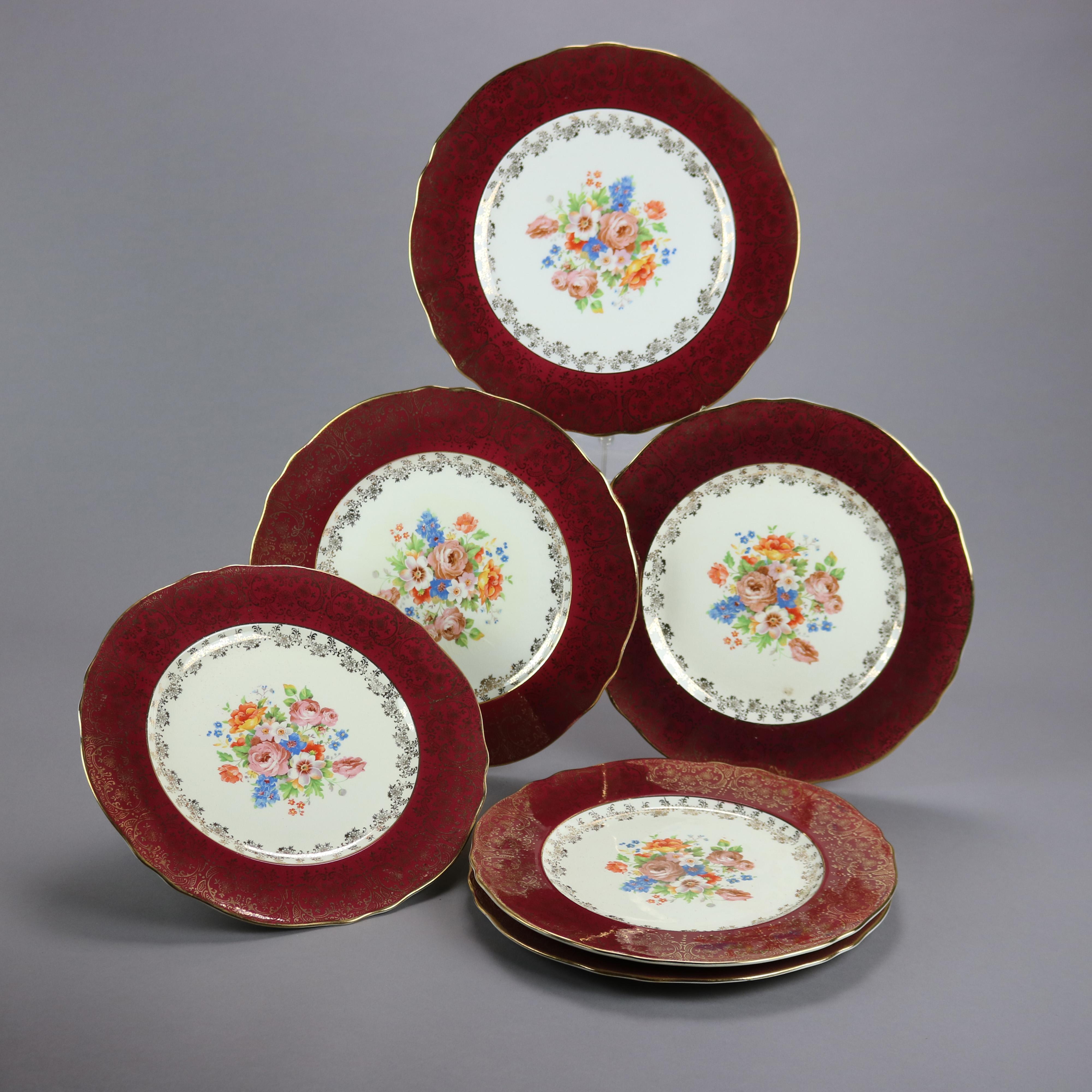 Un ensemble de six assiettes à dîner par Atlas China offre une construction en porcelaine avec un puits ayant un bouquet floral et un bord bord bordeaux avec une décoration dorée de feuillage et de rouleau, le timbre du fabricant sur les bases comme