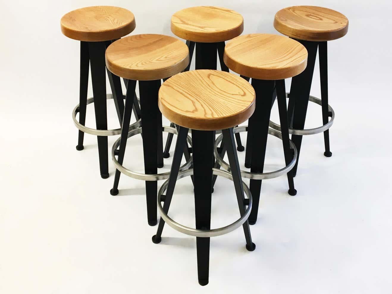 Six bar stools in black enameled metal, a brushed aluminum footrest, and a seat in hand-turned, stained oak with a slight concave in the center. They are an updated and improved version of Prouvé's 1952 design.
Diameter listed is the footrest's