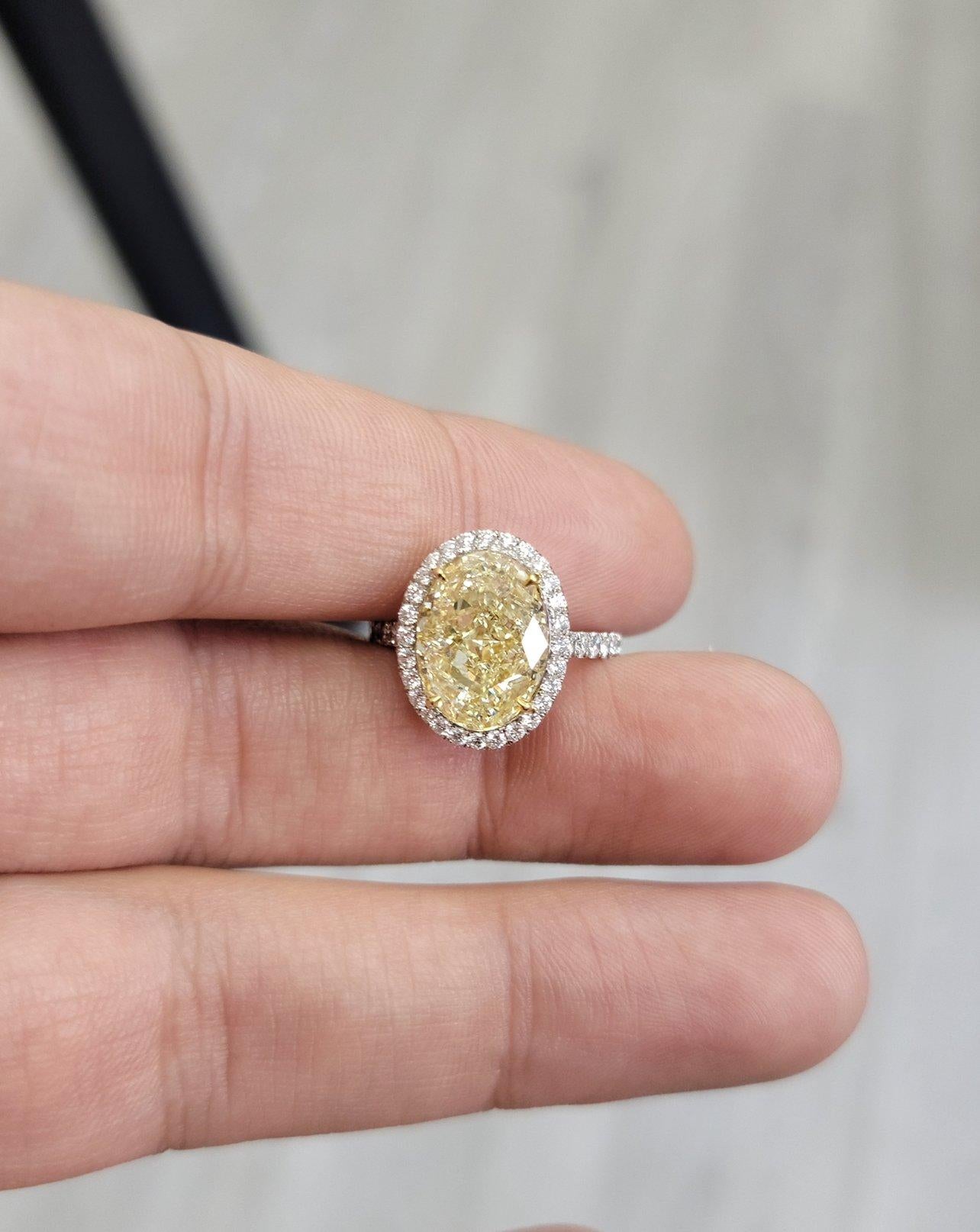Stunning 6.02 carat Natural LIght Yellow Oval Diamond in Platinum and 18kt yellow gold. 
Approximately half a carat of white round diamonds surround the gorgeous center oval.
Beautifully even Color Distribution and sure to be loved for generations.