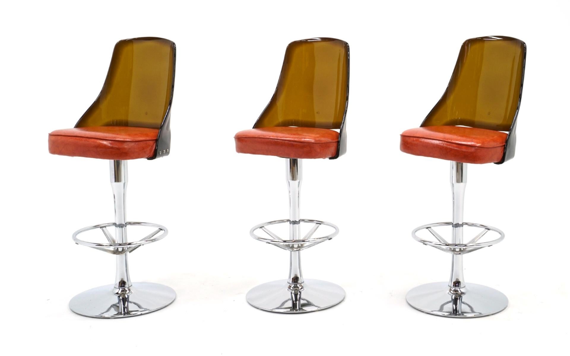 Four have sold, we have a pair available.  Acrylic and chrome barstool with orange seats in very good to excellent condition. Thick 3/8th inch amber colored Lucite backs and chrome stand with footrest. The orange vinyl seats look virtually like new.