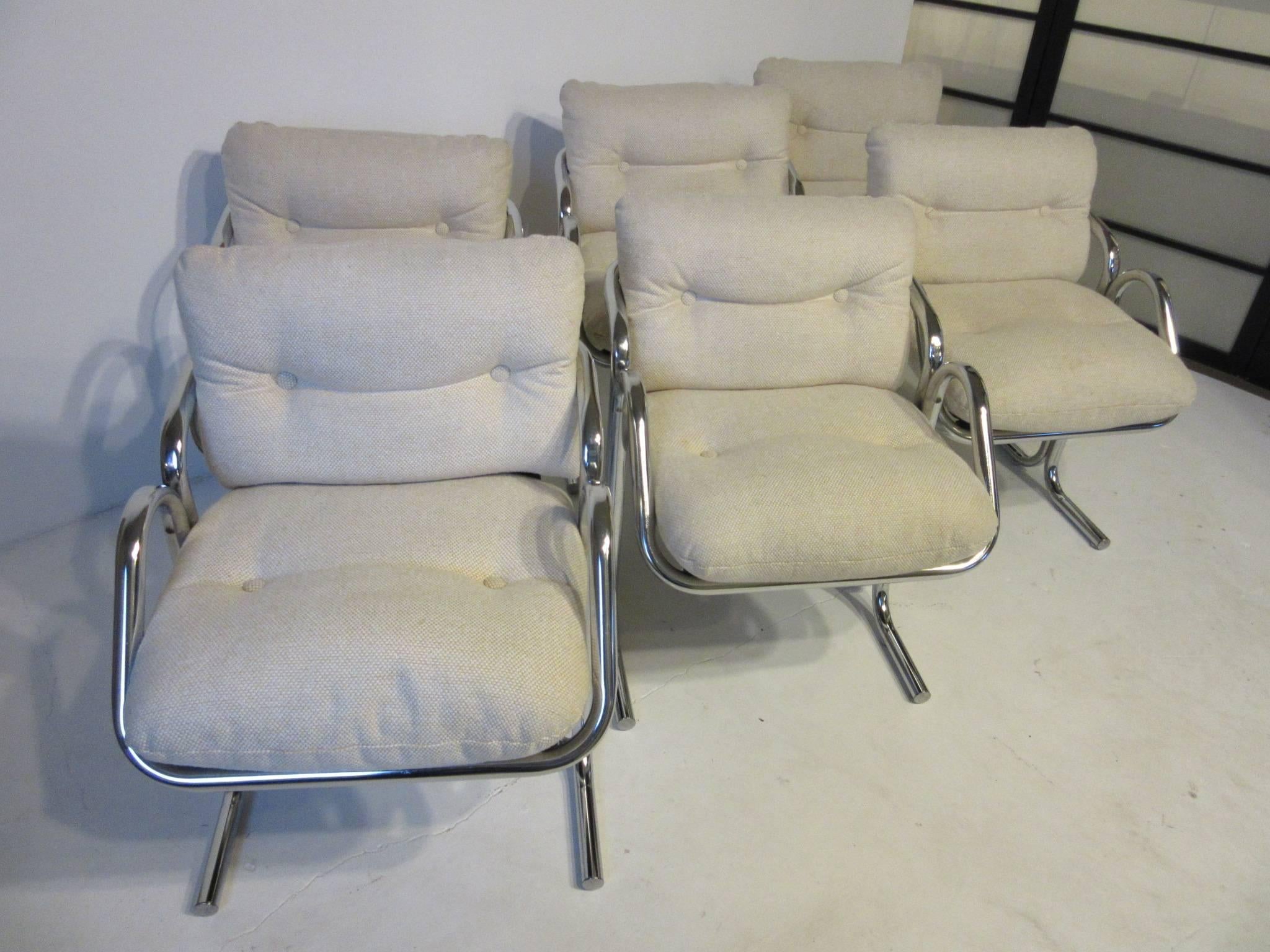 A set of six tubular framed armchairs with oat meal toned upholstery and buttons, the cushioned seat and back are supported by a canvas sling design for greater comfort. With the lower arm profile they can be tucked under many table tops both dining