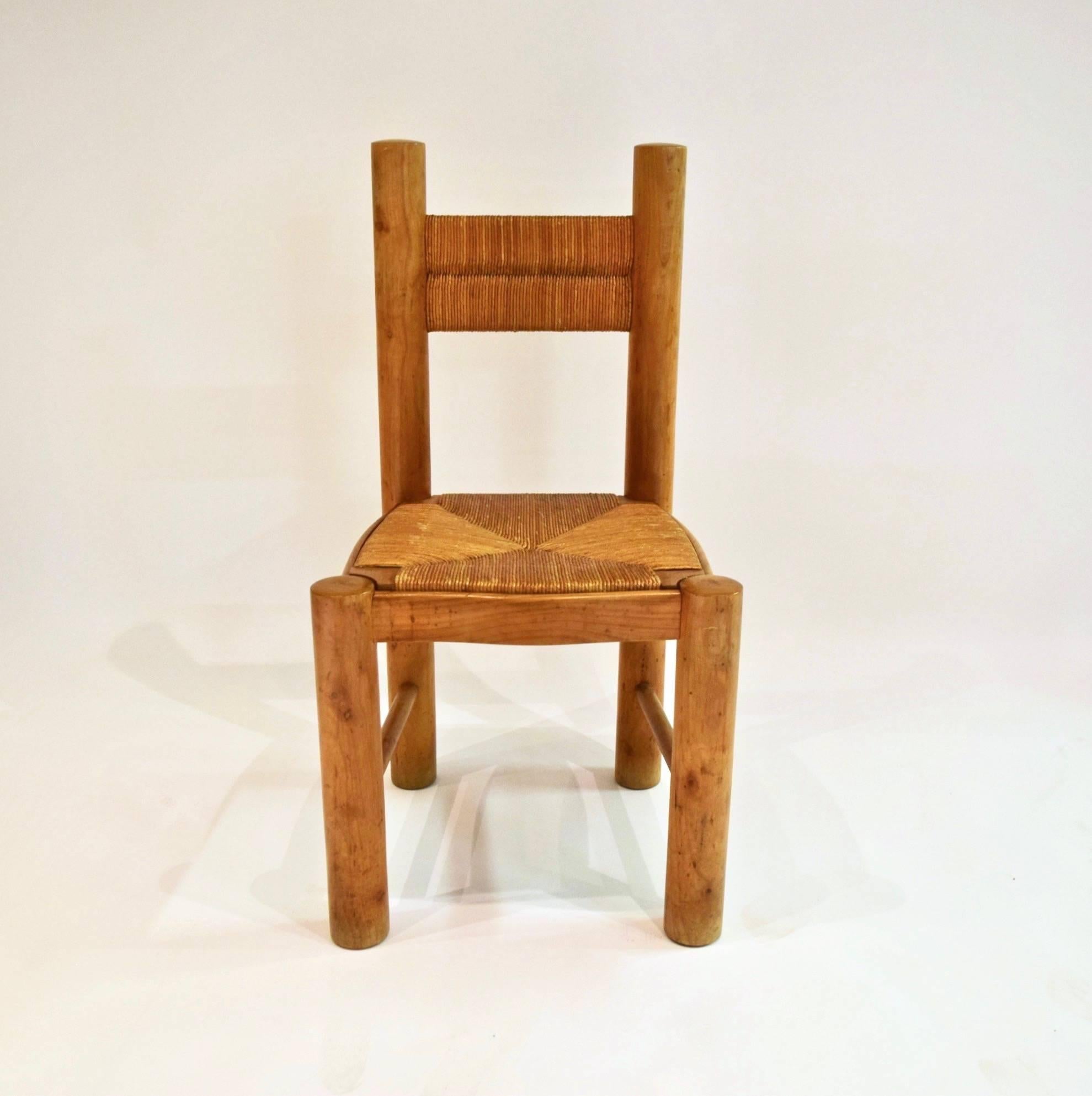 Six armless dining chairs by Jean Royère with rounded, cylindrical rush wood posts as the back and front legs, two perpendicular, cylindrical stretchers, a bowed and curved ash seat frame with an inset seat of woven rush, and a horizontal woven rush