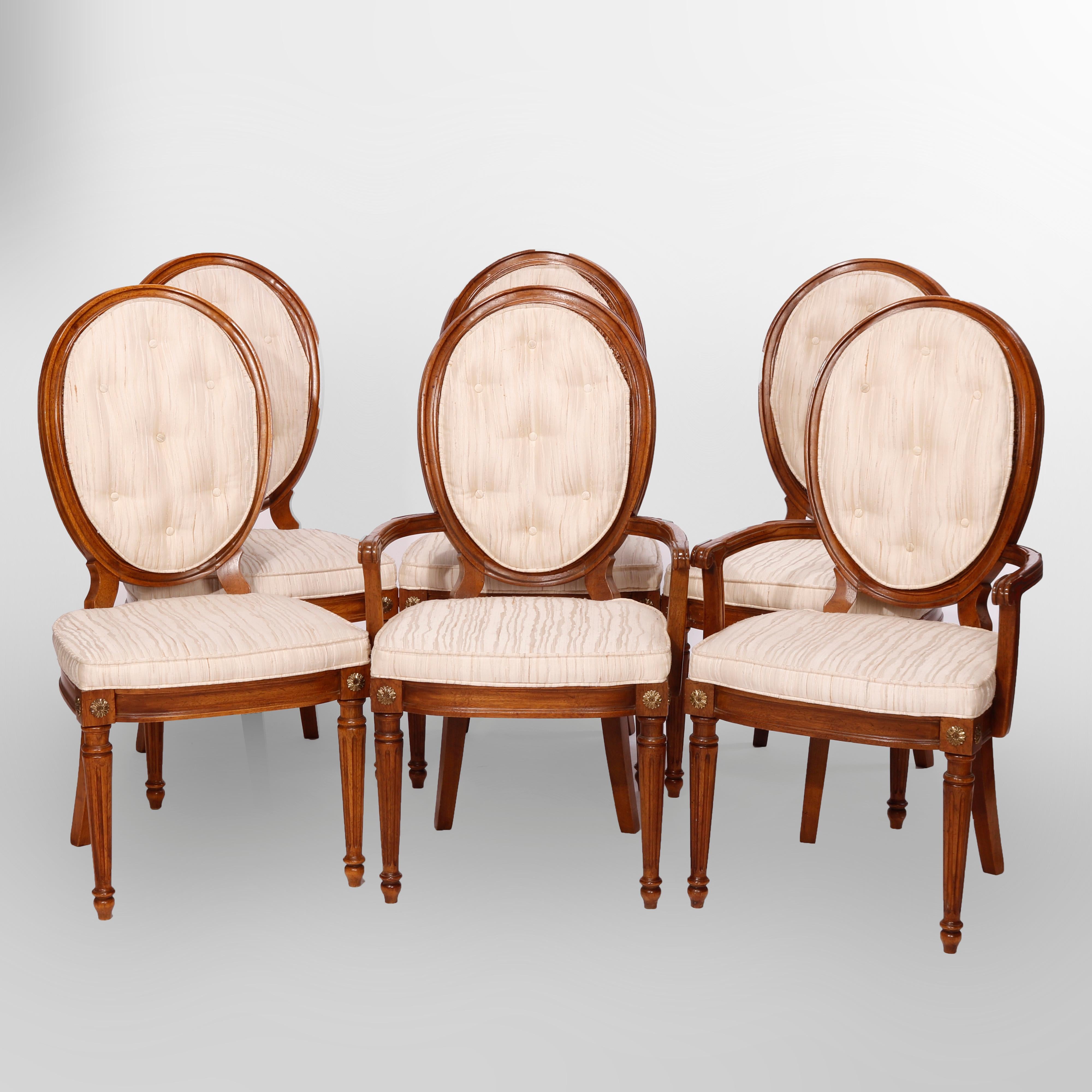 A set of six French Louis XVI style dining chairs offer walnut construction with medallion backs having pressed cane and upholstered button cushions over upholstered seats and raised on tapered and reeded legs having gilt rosette capitals, 20th