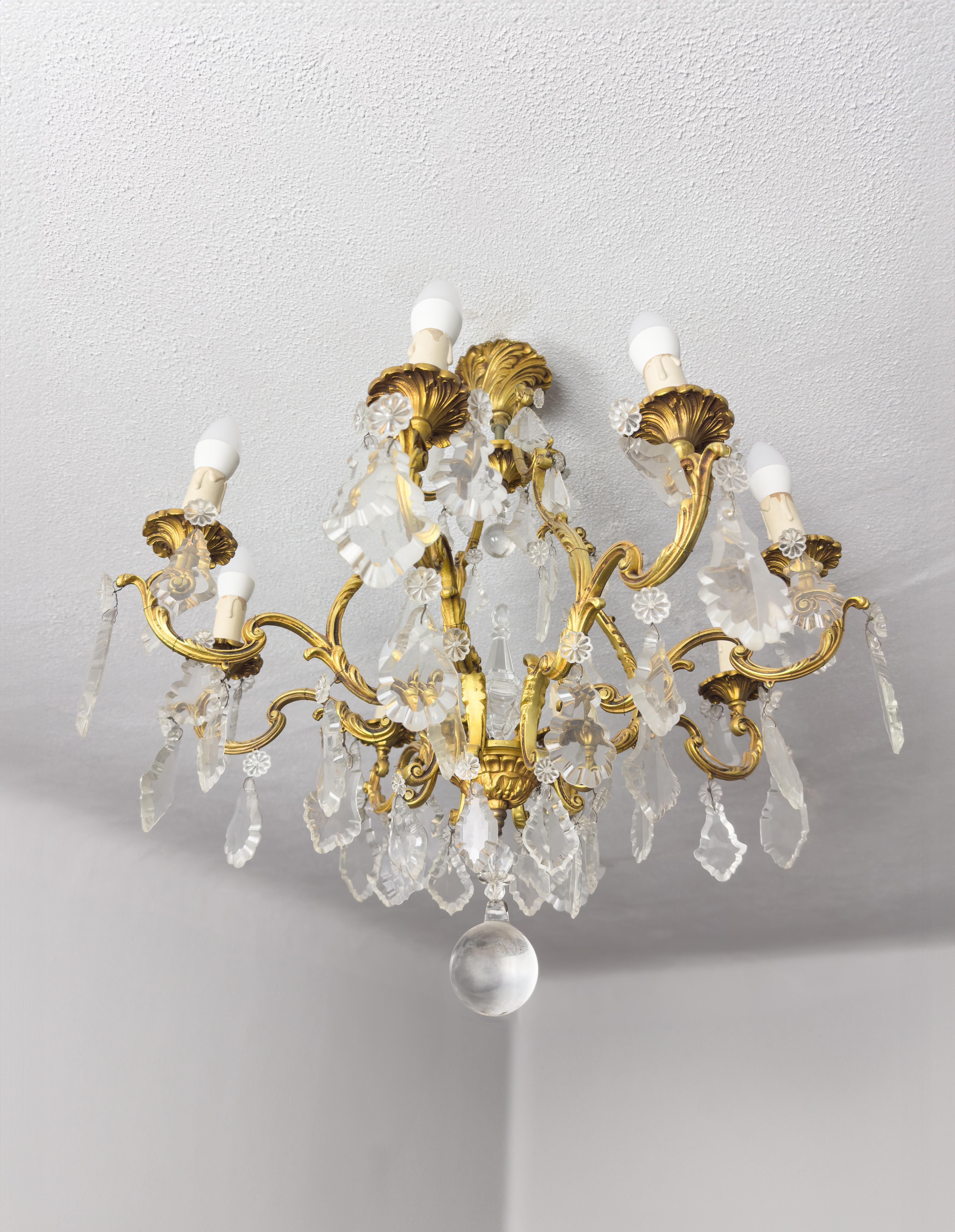 Lámpara de techo francesa de estilo Luis XV con volutas de bronce dorado adornadas con colgantes y remates de cristal facetado, con portavelas de seis ( 6 ) velas.

Sus seis luces se reflejan maravillosamente a través de los elementos de cristal