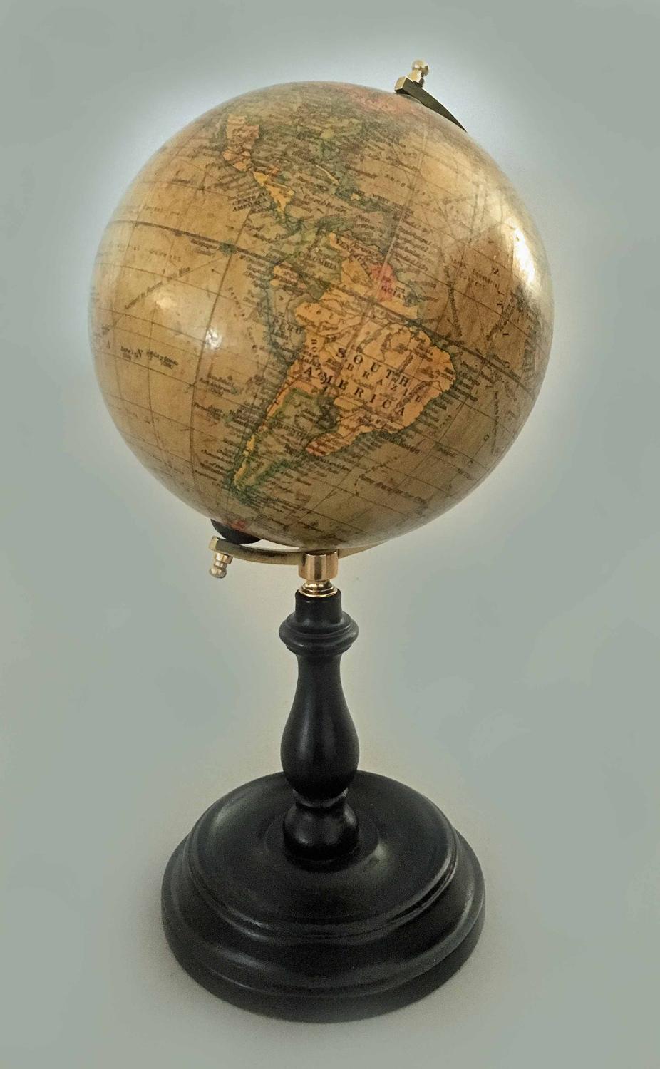 Six inch terrestrial desk globe held in place by a brass meridian mounted on an ebonized turned Stand, signed Geographia, 55 Fleet St, London.