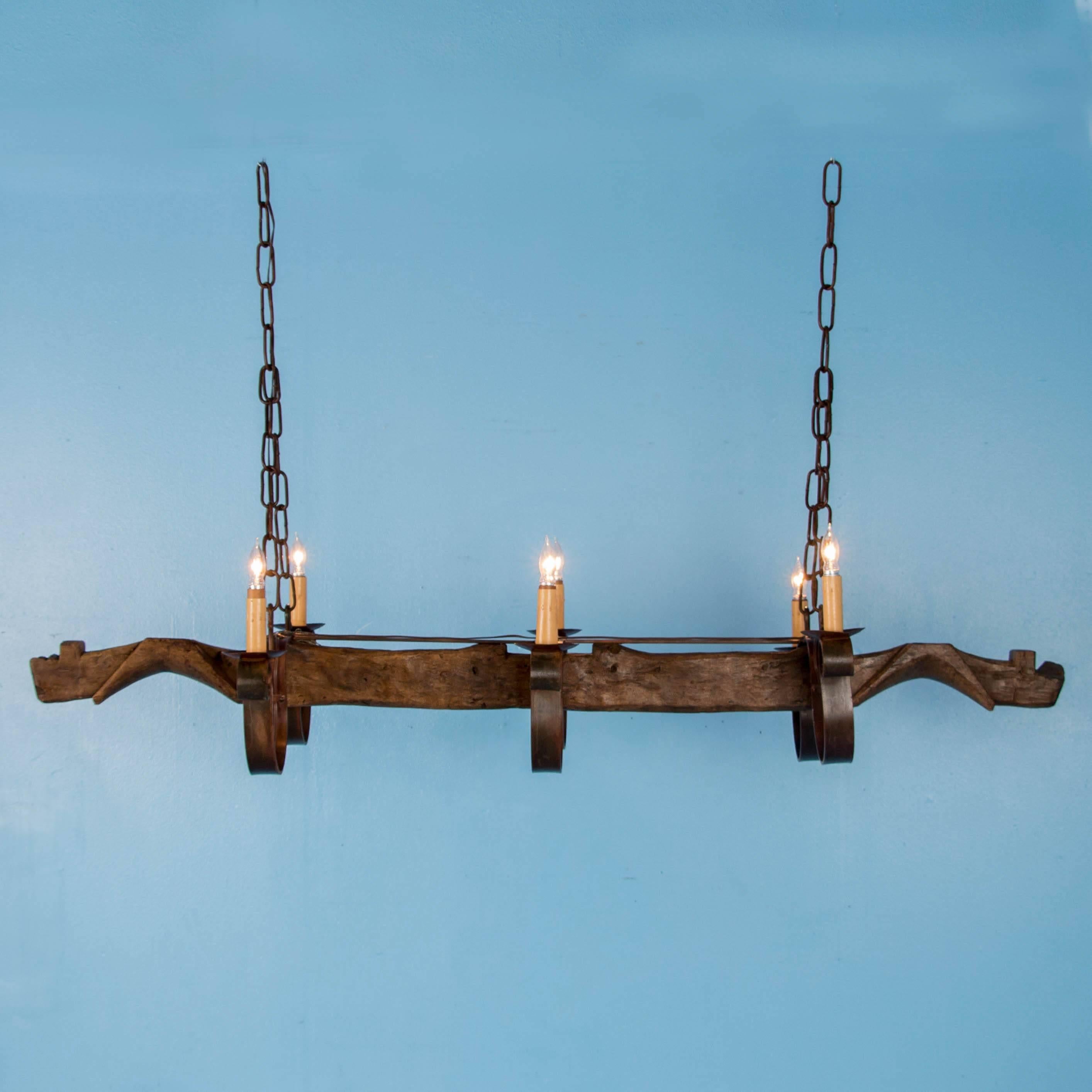 The vintage Mexican ox yoke made of oak, is the foundation for this long six-light chandelier. The rusted patina of the rolled iron arms and chain contribute to the rustic charm of this fixture. The chandelier has been sealed with a wax finish and