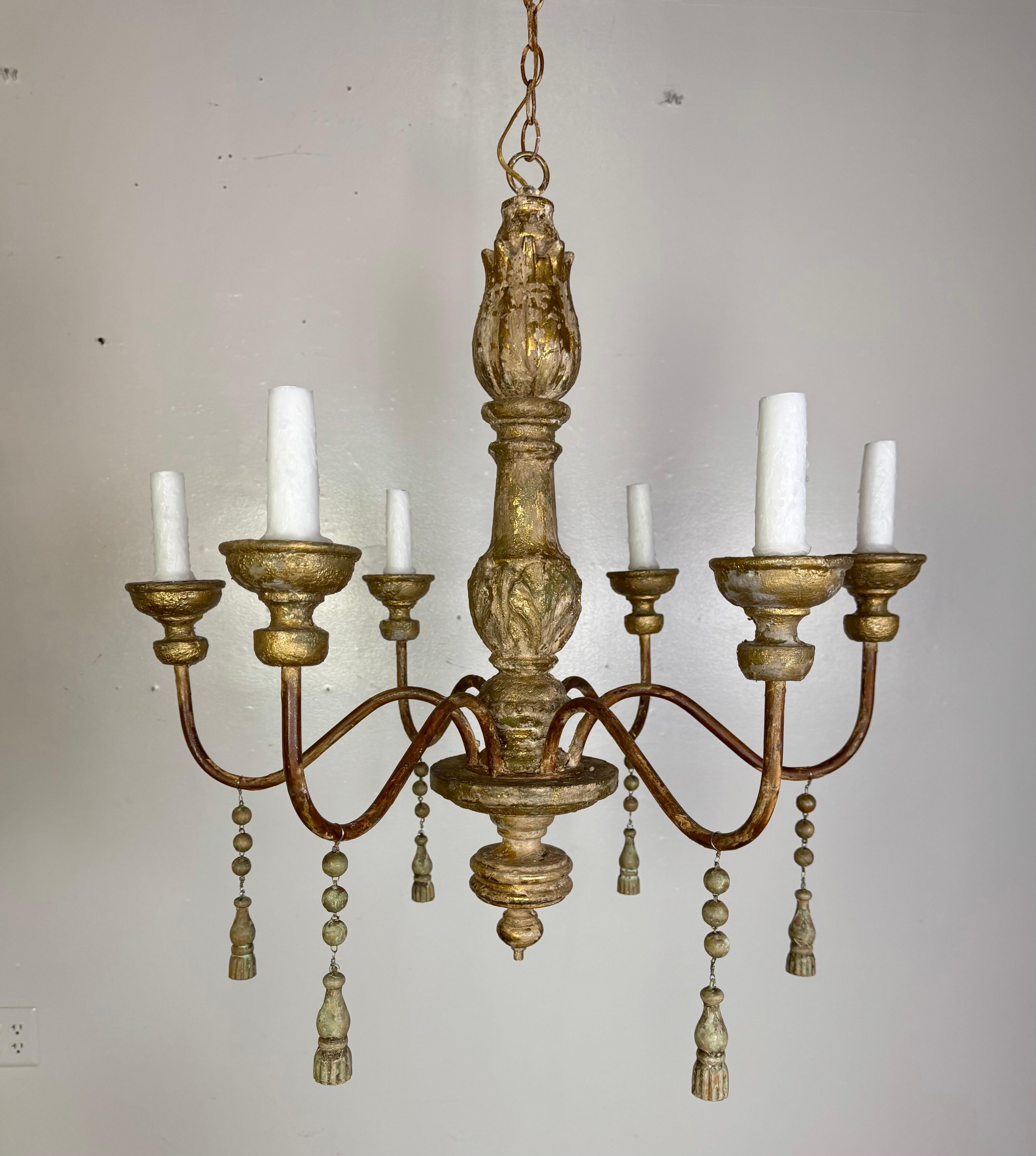 This elegant six-light Italian chandelier showcases classic European styling with a richly detailed silhouette and an aged, gilded finish. The central column features traditional turned wood with a carved tulip finial, beautifully worn to reveal