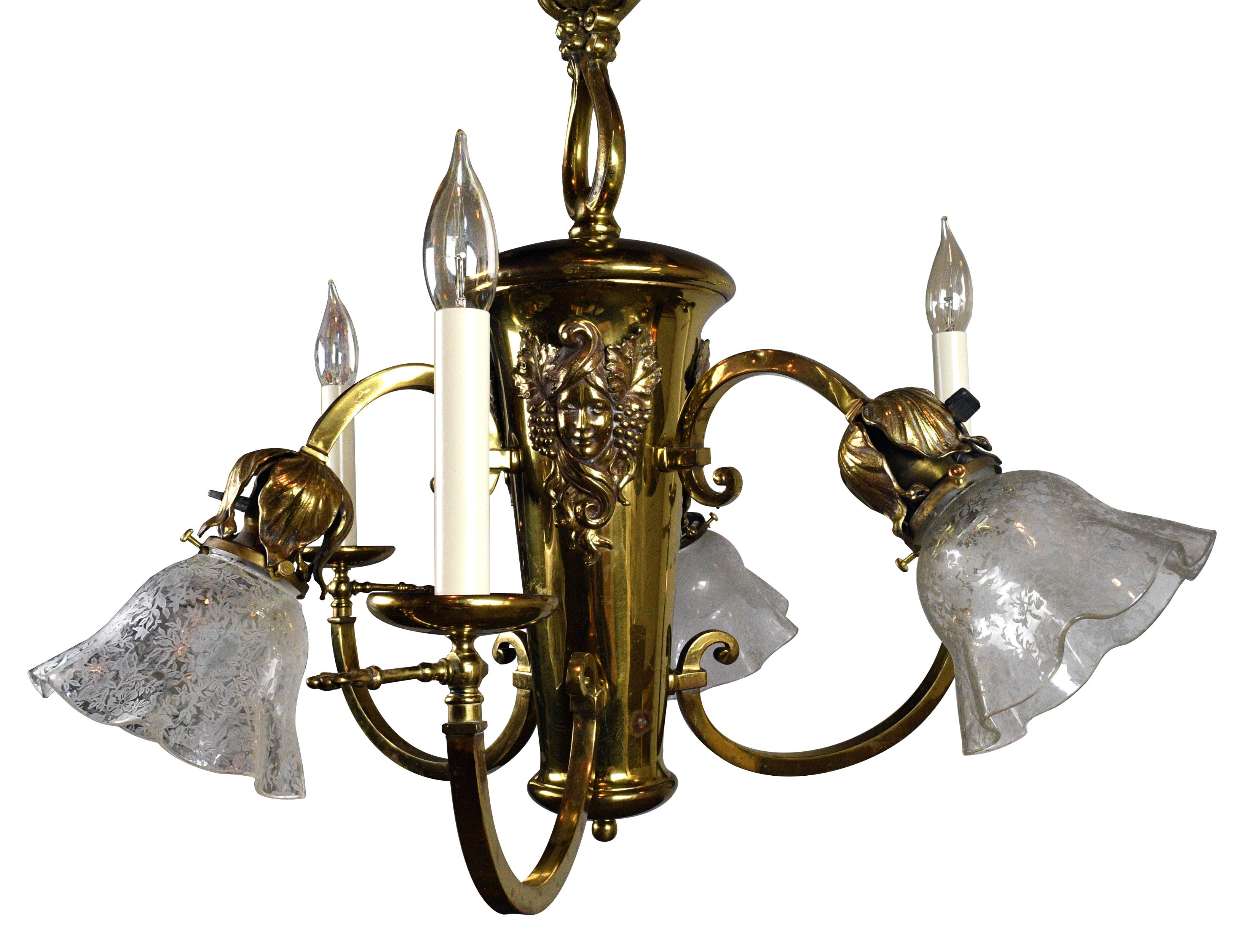 Brass chandelier with six arms — three with candles and three with shades. The chandelier features three cameos surrounded by grapes and leaves while the shades feature a delicate floral and leaf pattern. Formerly a gas/electric fixture, it still