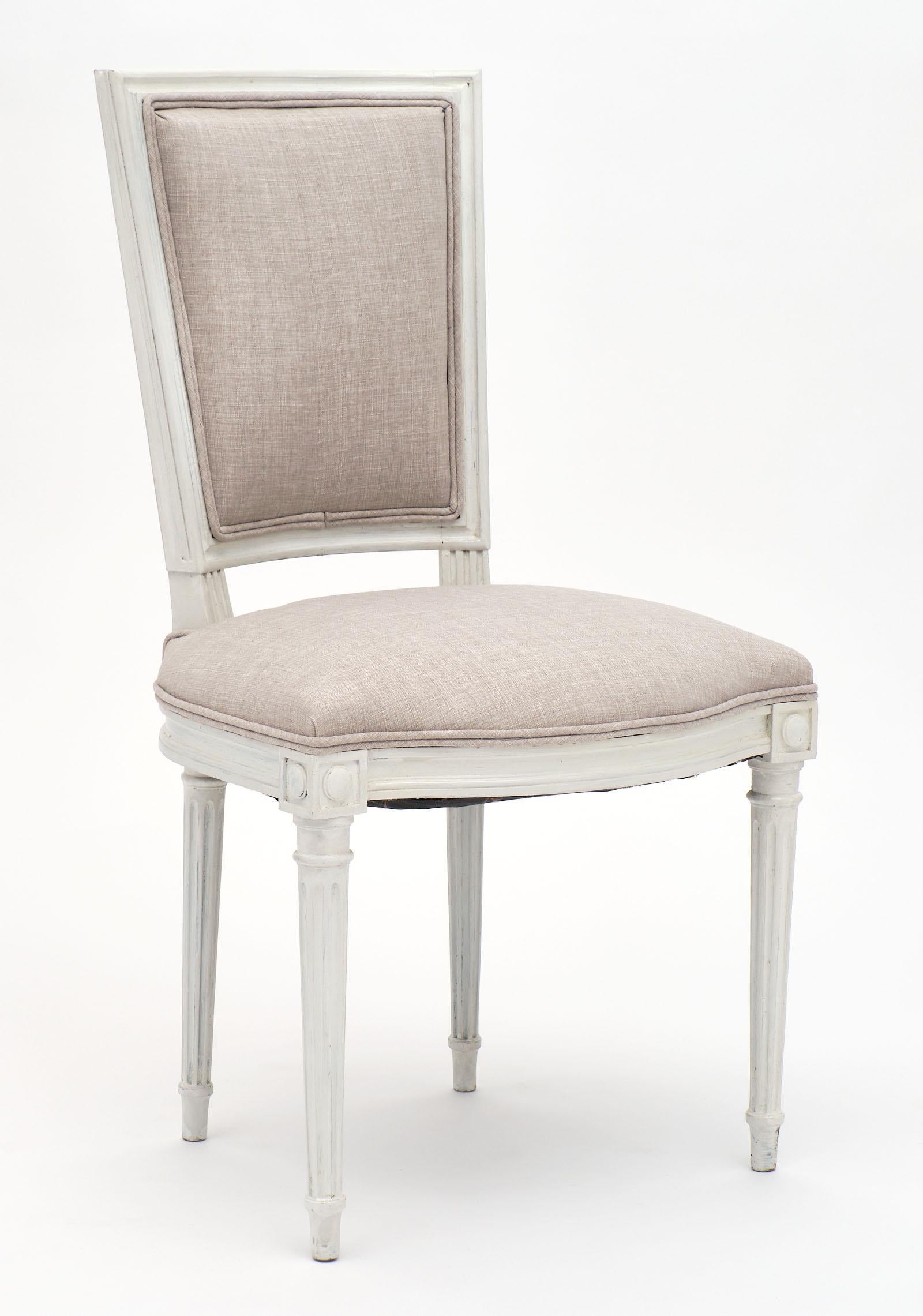 Set of six Louis XVI style painted dining chairs newly upholstered in a light gray linen blend. We love the beautiful straight lines of the back, the slightly curved support for comfort, and tapered and hand carved fluted legs. The trianon gray