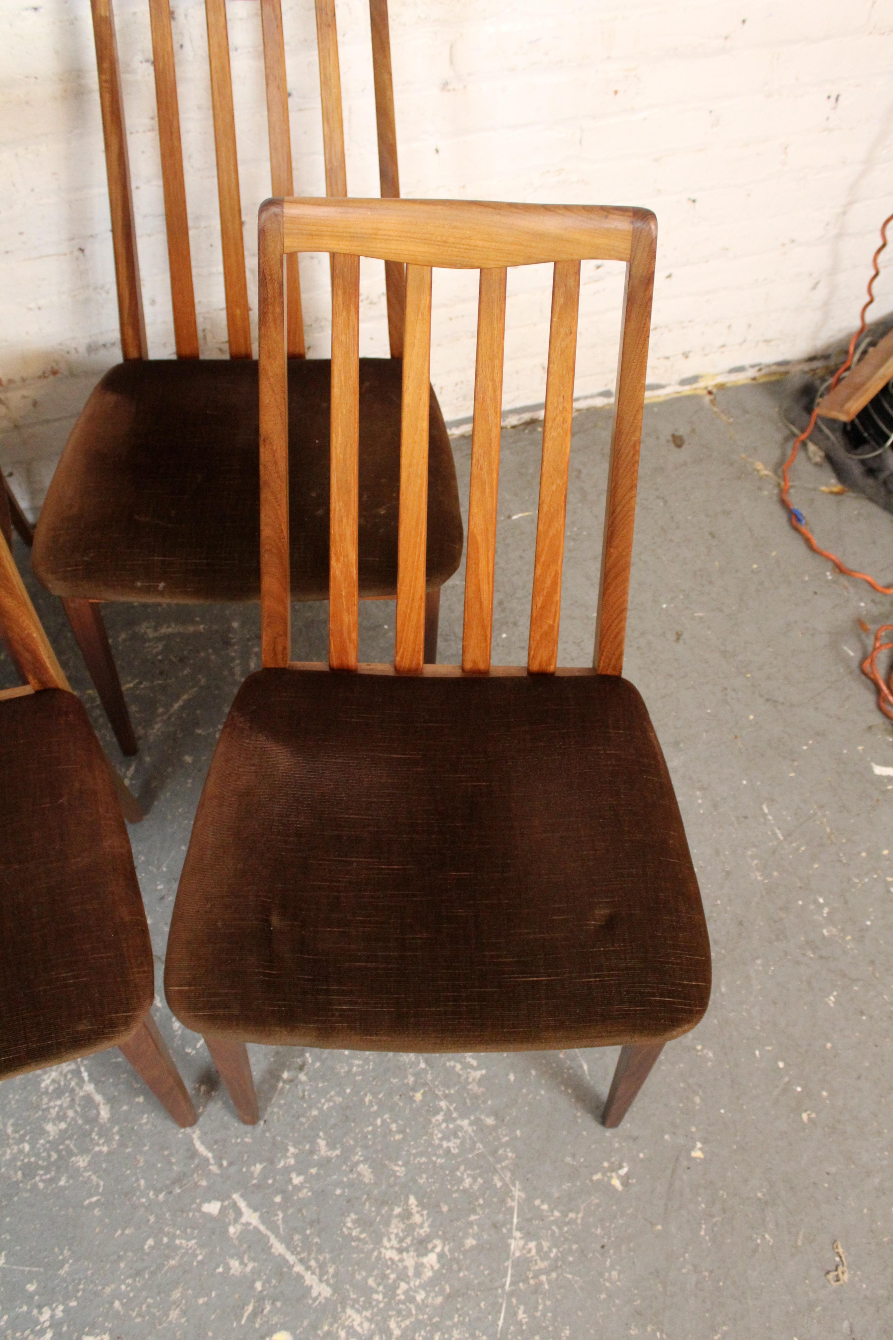 Fabriquées en teck aux tons chauds et miels, ces chaises aux proportions élégantes sont dotées d'un dossier à lattes sculptural et de pieds fuselés. Les sièges originaux ou nouvellement rembourrés offrent confort et style, ce qui en fait un