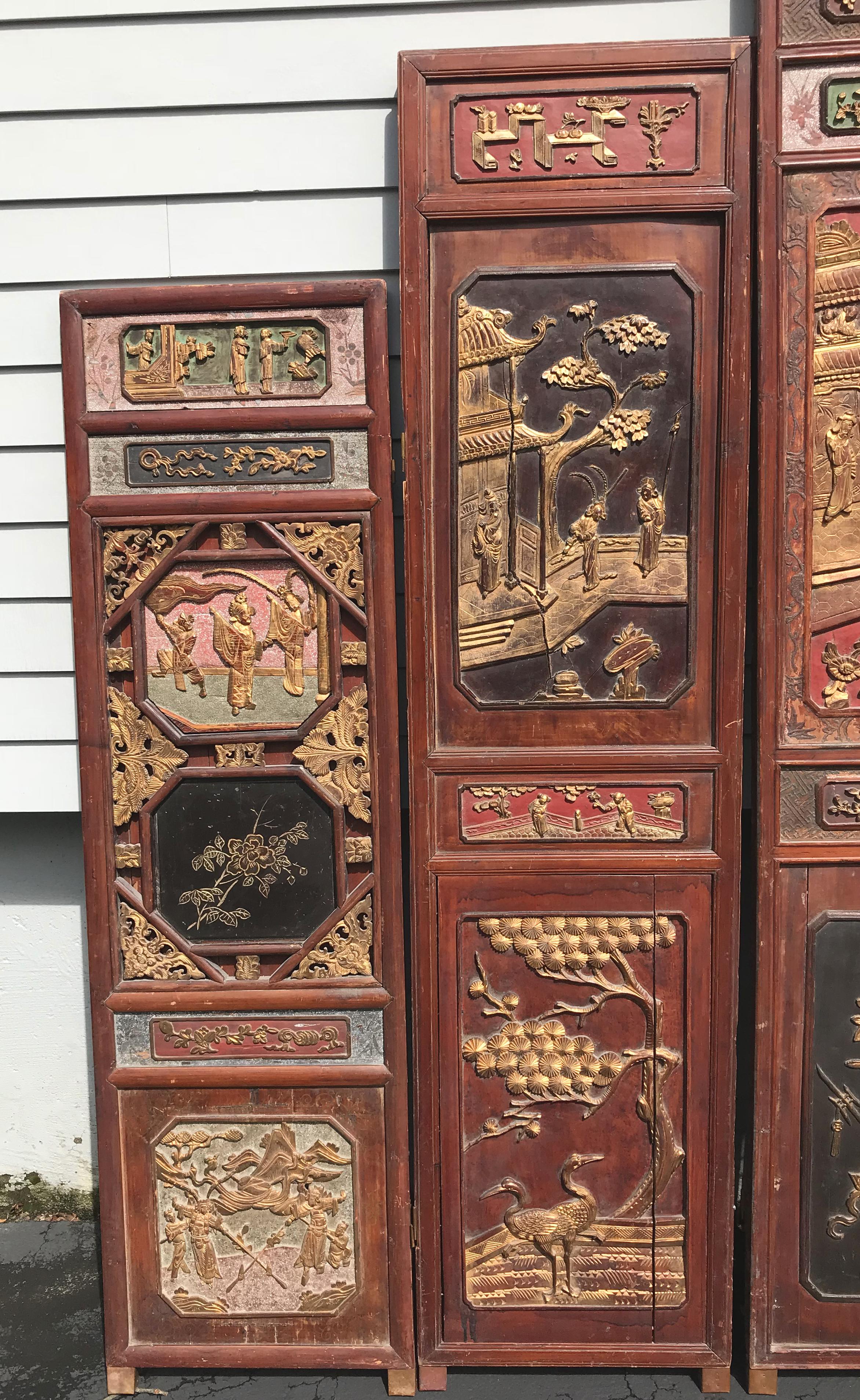 An assembled decorative six-panel carved Chinese wooden dressing screen with polychrome and gilt decoration, each panel depicting various folklore scenes, trees, and animals, with graduated sizes and brass hinge hardware, dating to the late 19th or