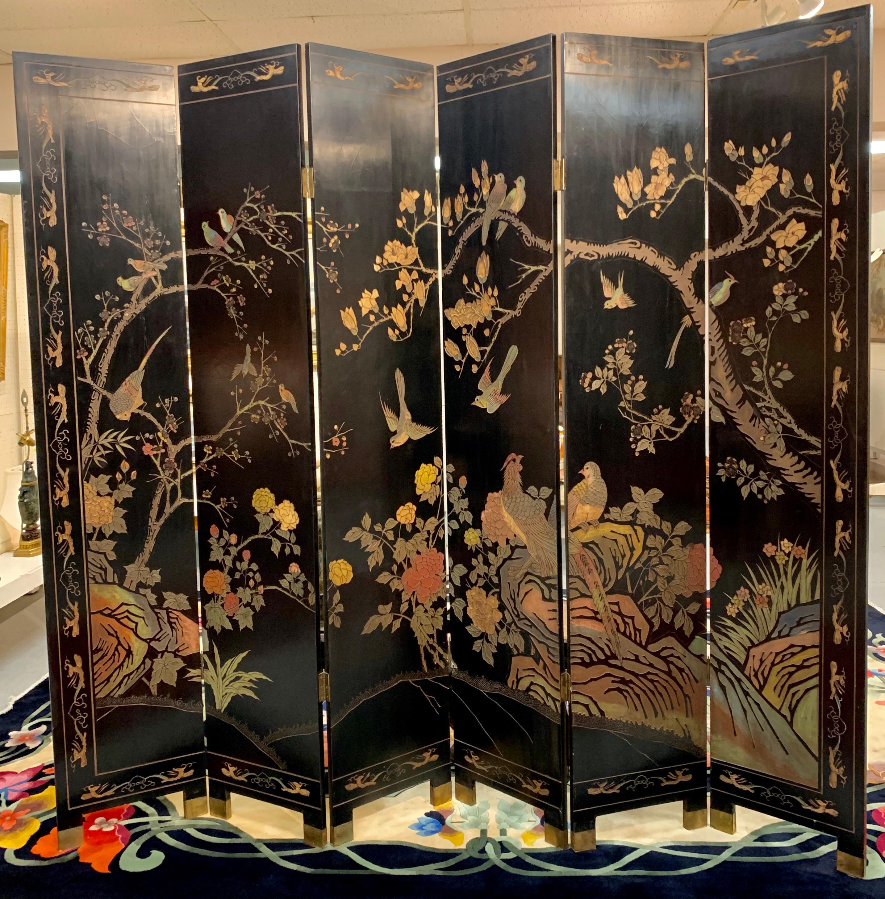 Magnificent seven foot tall six panel chinoiserie coromandel screen that is double sided and features lacquered wood with carved designs on both sides. Hints of many colors on each side and featuring two brass capped feet on each panel. One side