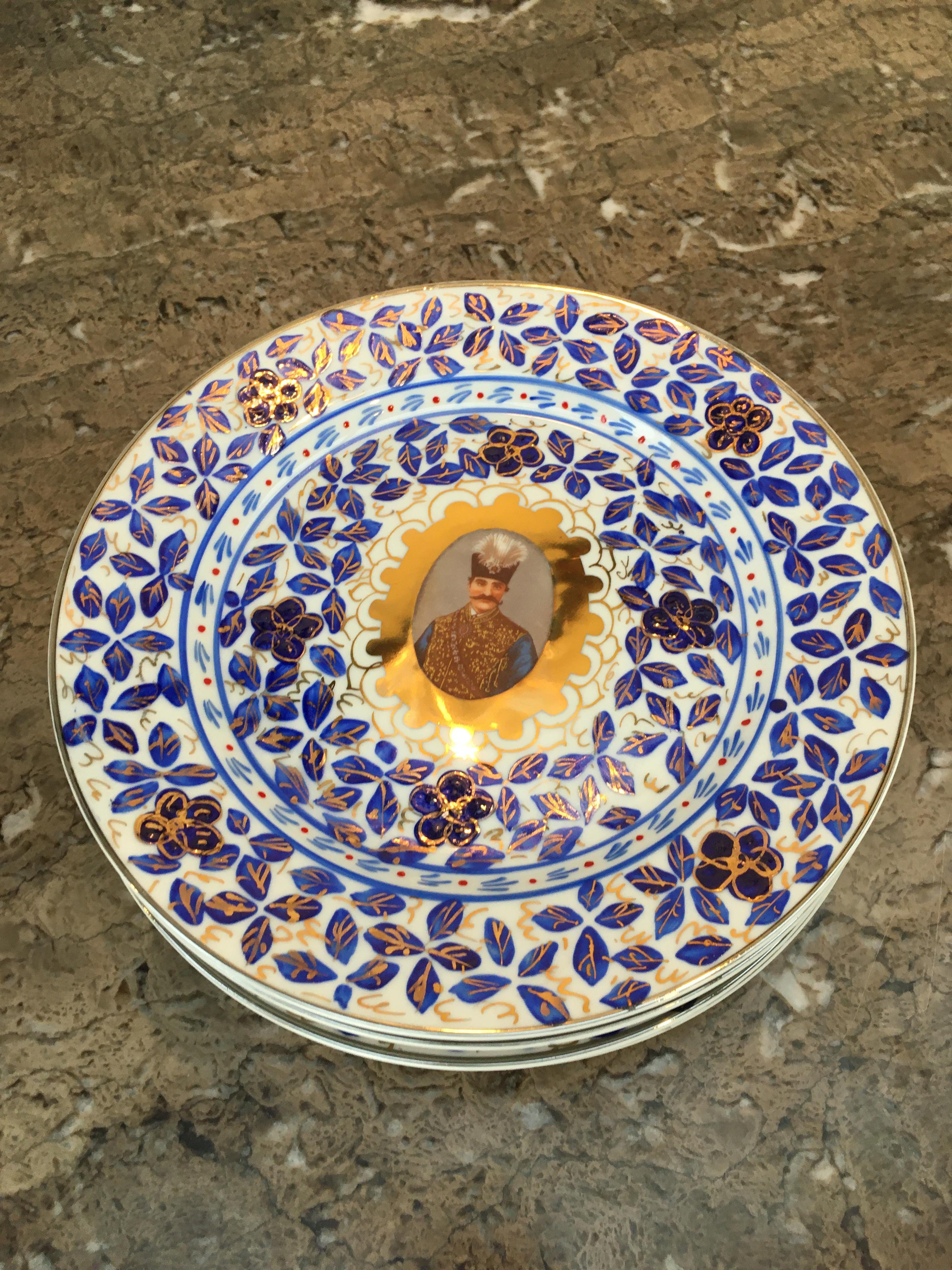Ein Satz von sechs Tellern mit Gedenkporträts von Naser al-Din Schah Qajar. Das Ganze ist von Hand mit einem traditionellen Muster aus Blättern, Blumen und Vögeln in Kobalt überglasiert und anschließend paketvergoldet. 

Dieses seltene Porträtset