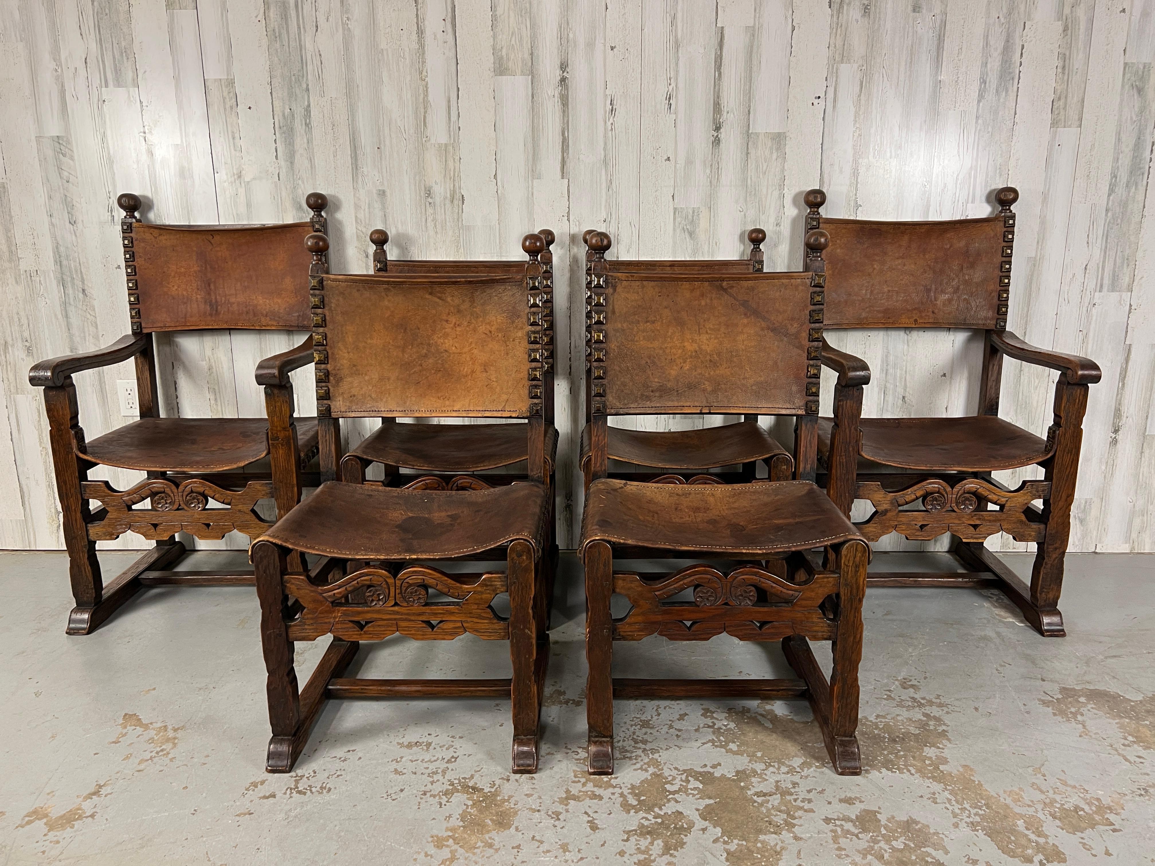 Set of six antique rustic Renaissance style solid oak hand carved dining chairs with thick saddle leather and large brass decorative studs. Nice patina on the leather and wood.
 Arm chairs measure 22,5 deep by  23.3/8
