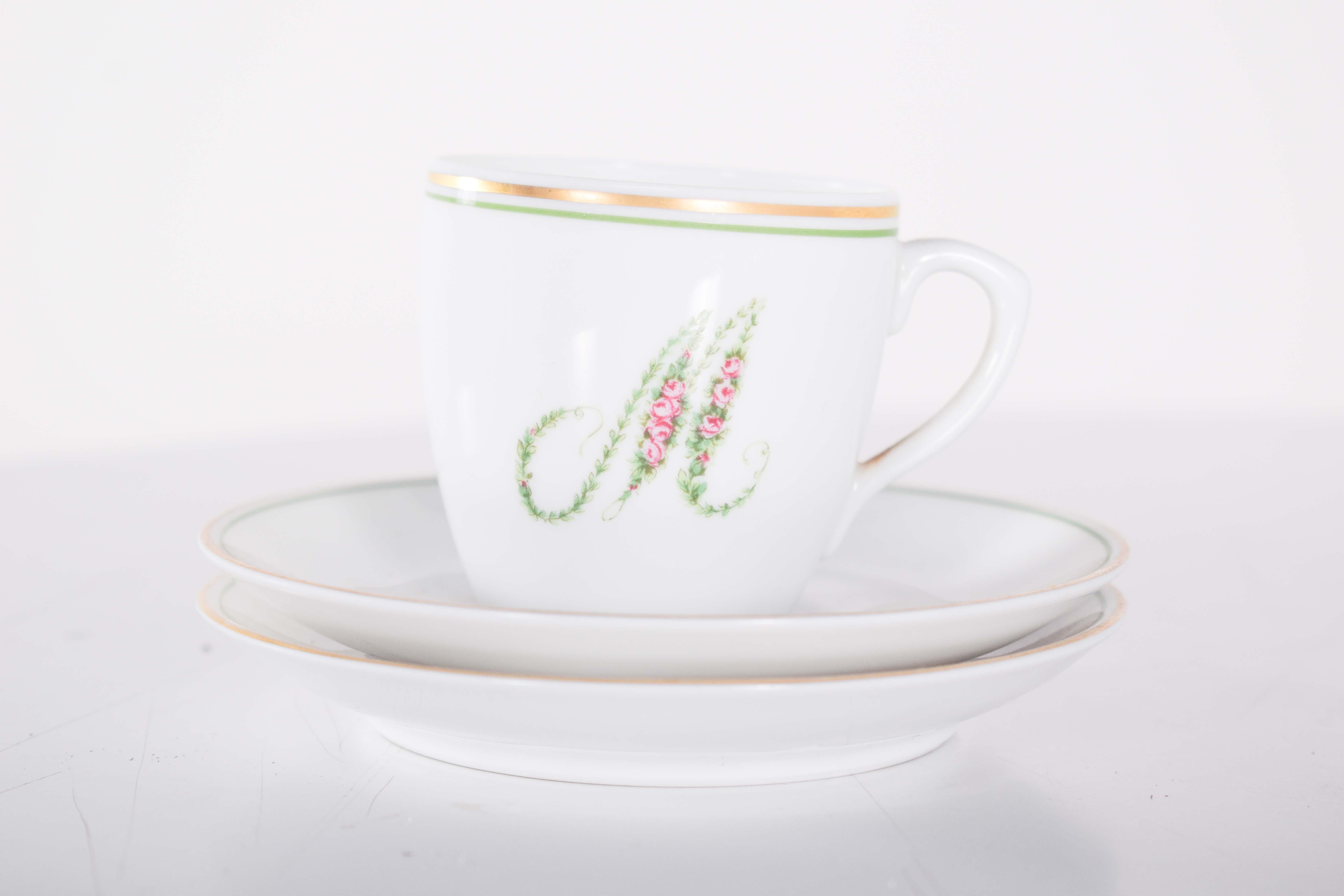 Sei piattini e tre tazze da caffè, in porcellana bianca di Vista Alegre, decorati con lettere, fiori sulle lettere e finiture in oro. Entrambi sono caratterizzati da lettere, decorate con morbidi motivi floreali nei toni del rosa e del verde, che