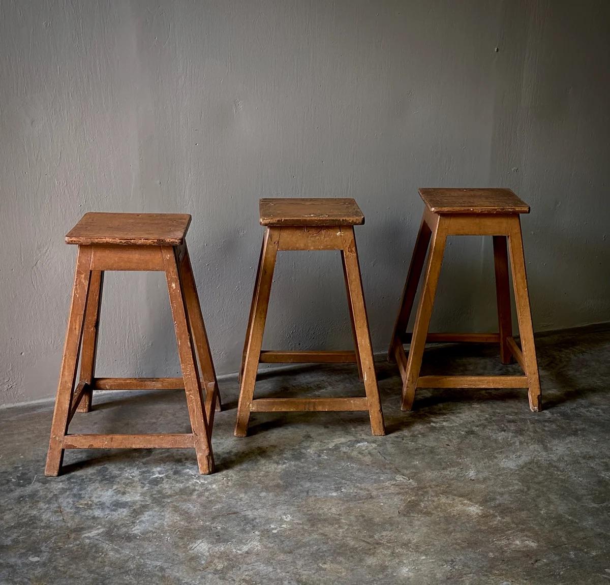 Trois tabourets d'usine en bois datant de la fin du XIXe siècle en France présentent une patine fantastique due à l'âge et à l'utilisation. Avec une assise carrée et des pieds en forme de blocs reliés de tous les côtés par un brancard ou un