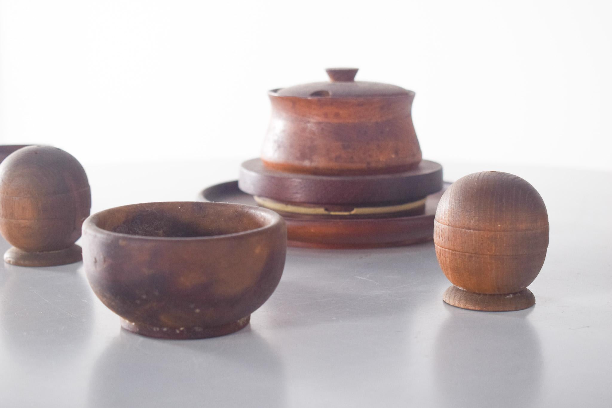 Six small, miscellaneous pieces made of wood. The set consists of a sugar bowl with a lid and circular base, a salt shaker, a spherical pepper shaker with a flat base, and a wide-mouthed bowl and two smaller ones suitable for butter, jams, or