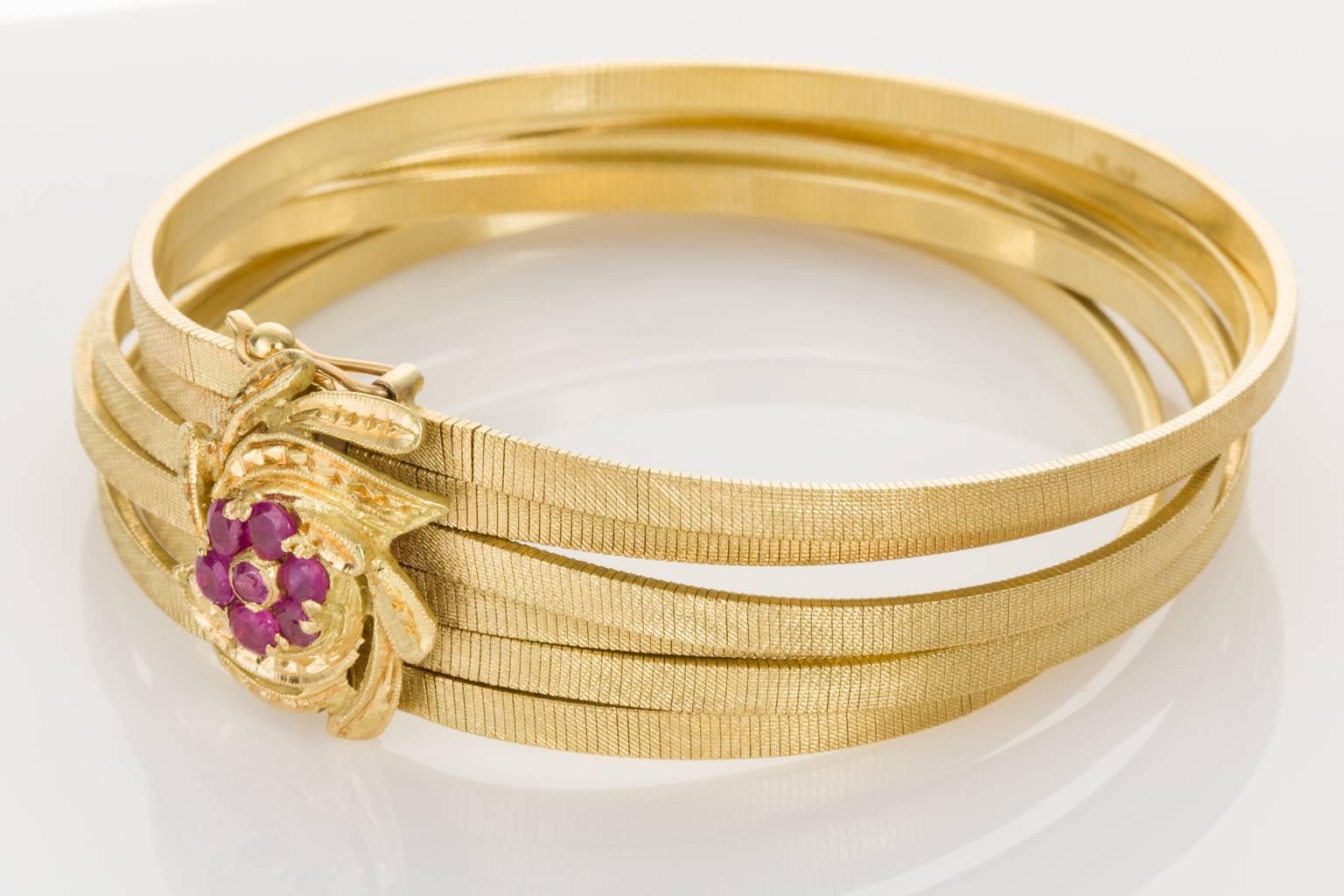 Nearly like liquid gold, these six 18k yellow gold strands have a beautiful sheen and are so smooth and fluid on the wrist. Fastened with a gold rosette motif centred with a flower of 7 round cut pinkish/red rubies, it's elegant and stylish for any