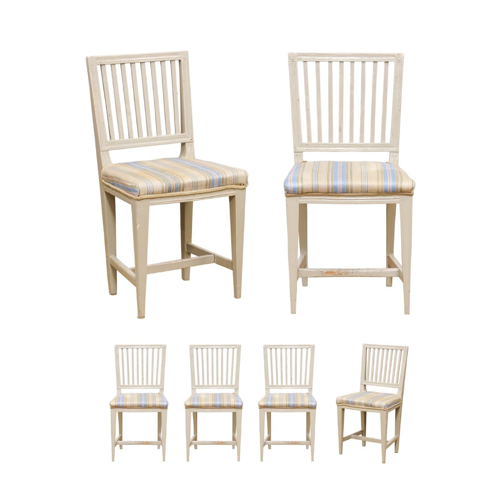 A set of six Swedish Gustavian style painted wood stick back side chairs from the mid 19th century, with tapered legs, carved rosettes and used upholstery. Created in Sweden during the 1850s, each of this set of six side chairs features a