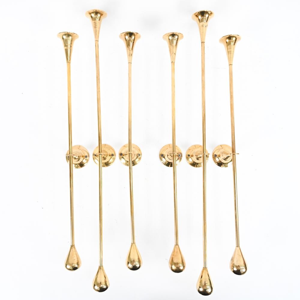 A stunning set of six Swedish mid-century wall-mounted candle holders in brass. These striking candle sconces are in the manner of Pierre Forssell's iconic candlesticks and featuring trumpet-mouthed candle holders with teardrop bottoms. A fabulous