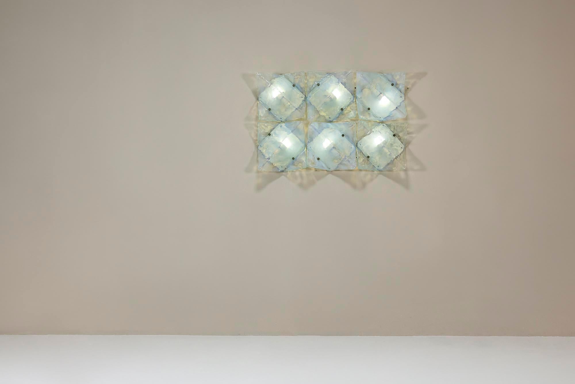 Each LP 253 lamp is crafted in a square form, made from ghiaccio-style opaline Murano glass, which gives it a frosted, textured appearance. The glass subtly softens the light, creating a gentle, diffused effect. Produced by AV Mazzega and featured
