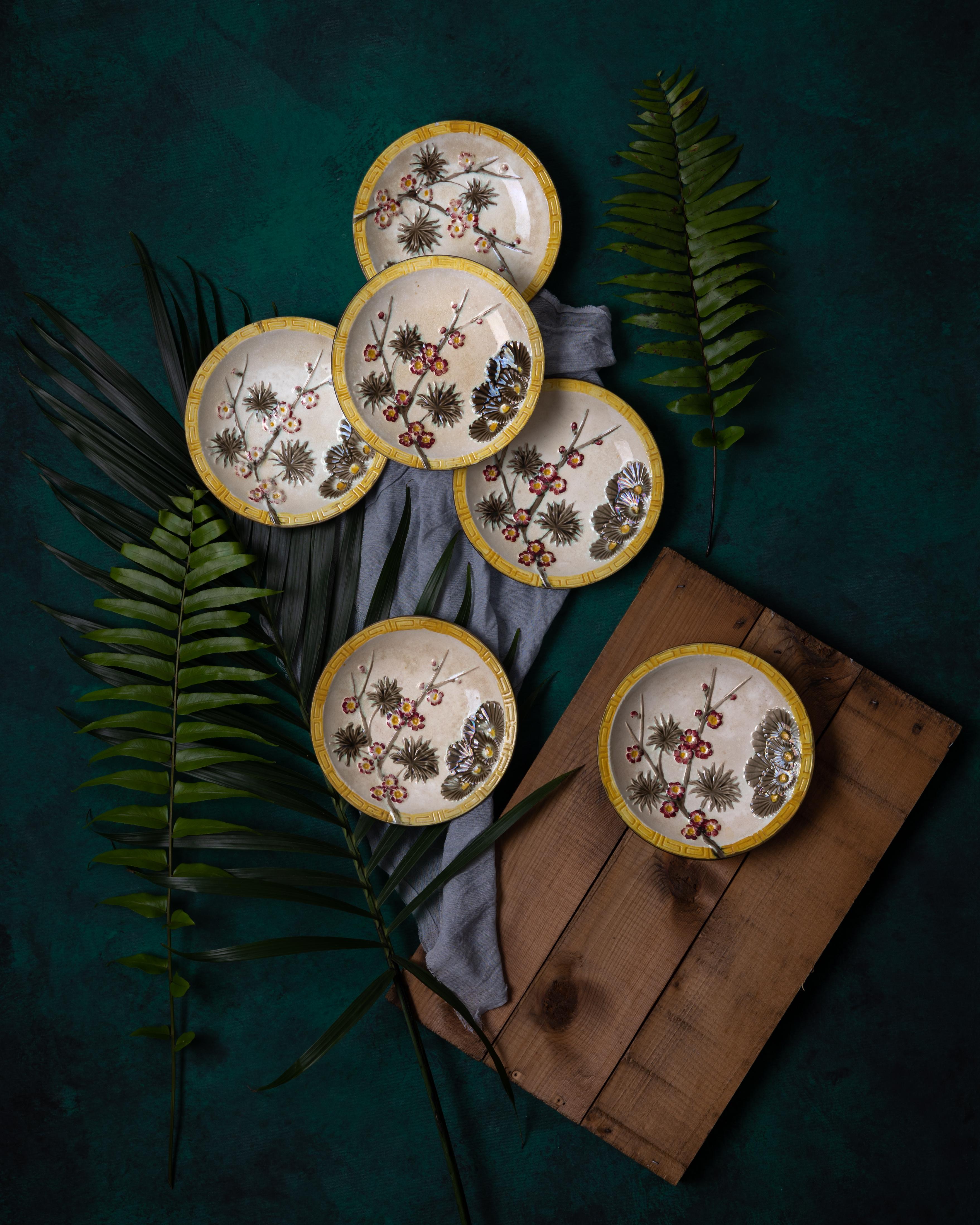 Six Wedgwood majolica Argenta palette ‘Lincoln' pattern dessert plates with finely molded maroon prunus blossoms and dark taupe pine branches surrounded by a yellow Greek key border. The dishes are decorated in the japonisme style and feature the